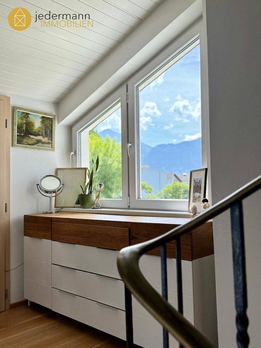 Heller Treppenabsatz mit Kommode, Dekoration und Bergblick durch das Fenster.