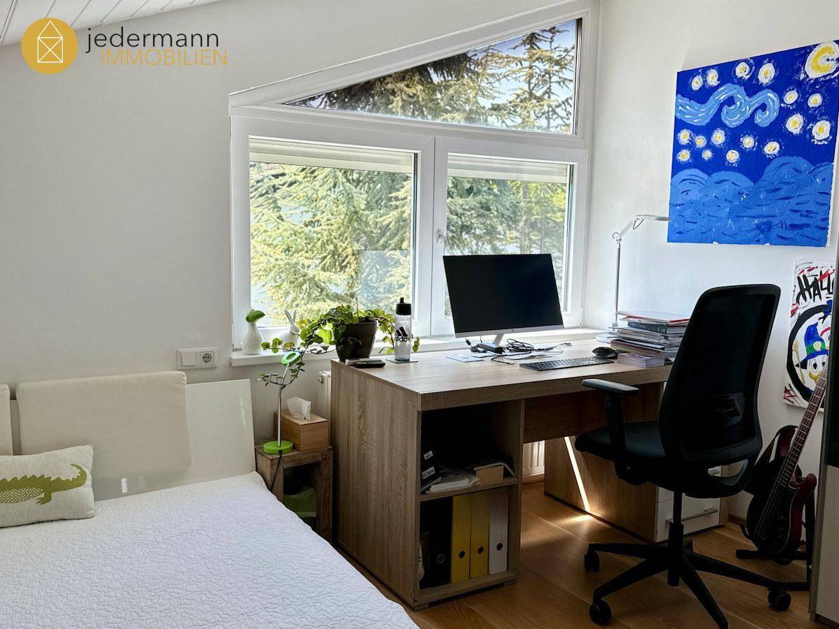 Helles Arbeitszimmer mit Schreibtisch, Bürostuhl und großem Fenster mit Blick ins Grüne.