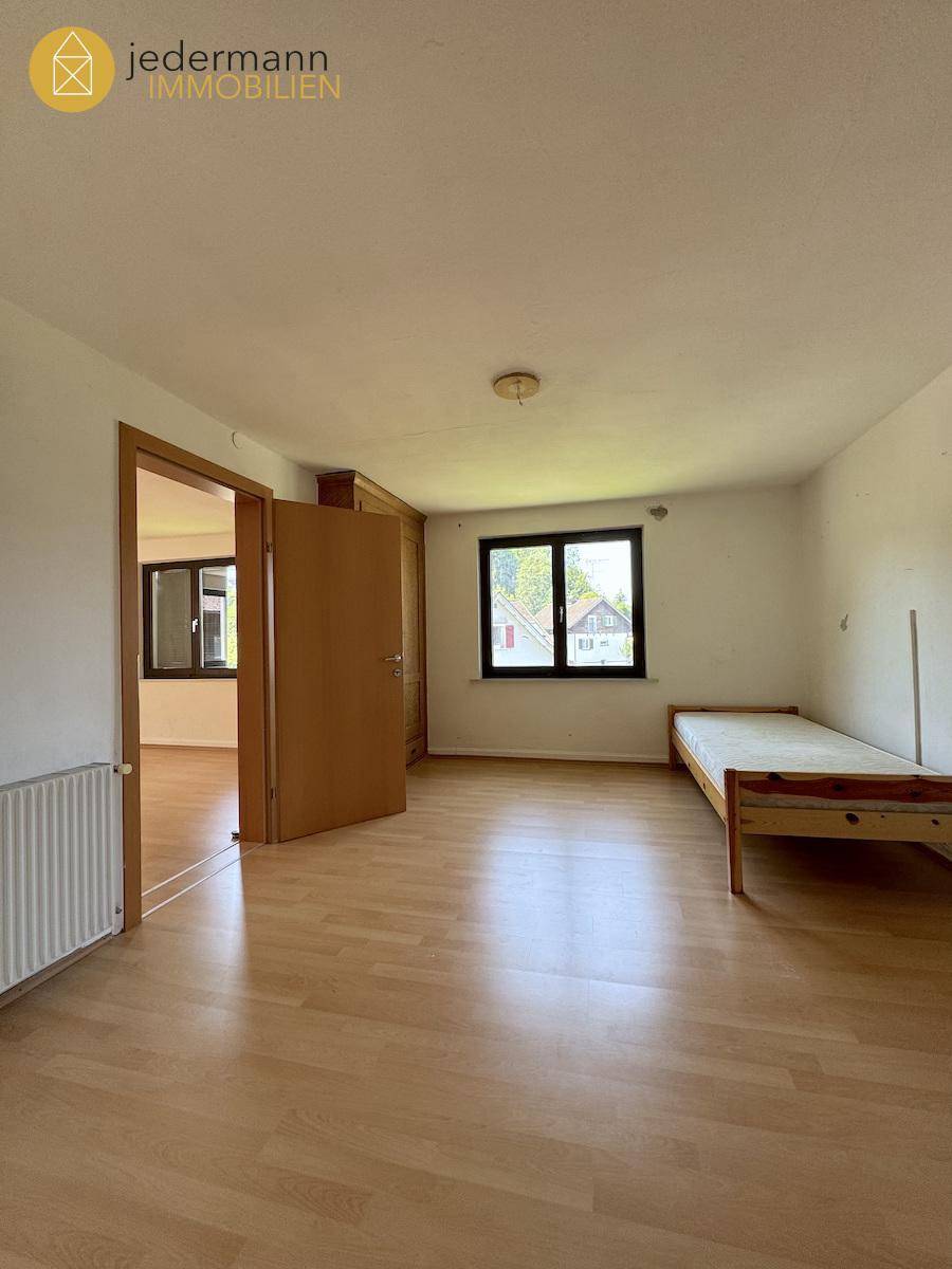 Geräumiges Schlafzimmer mit Holzboden, Fenster und einem Bett, das auf den Garten blickt.
