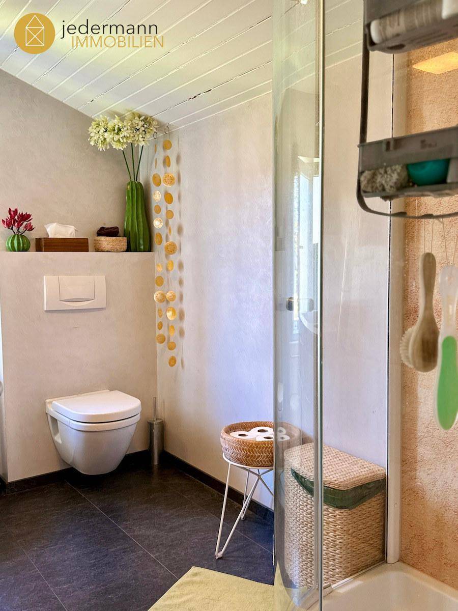 Modernes Badezimmer mit wandhängendem WC, Dusche und dunklen Bodenfliesen.