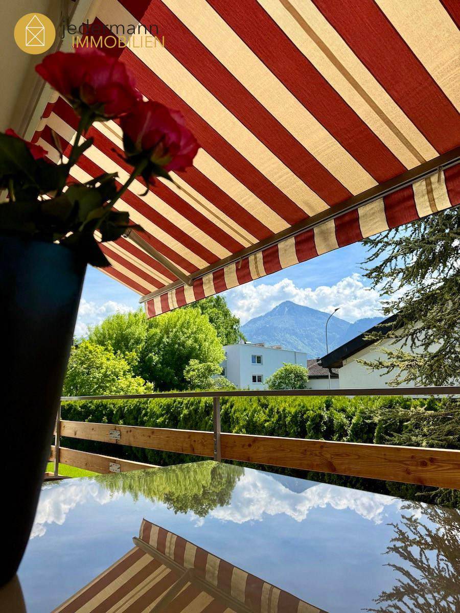 Sonniger Balkon mit Markise, Tisch und Stühlen sowie Bergblick.