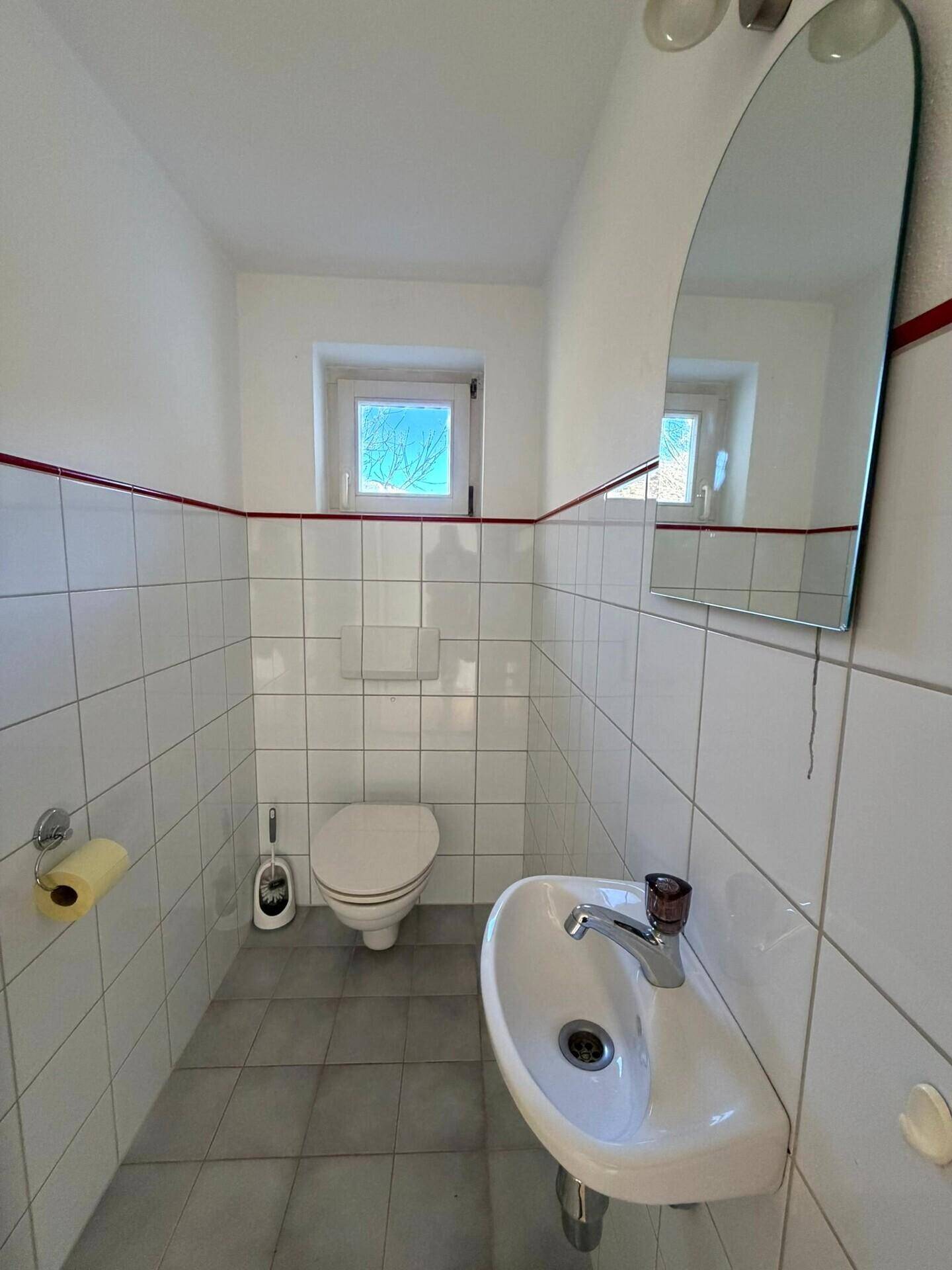 Separates Gäste-WC mit Waschbecken, Toilette und weißen Fliesen, inklusive Fenster.