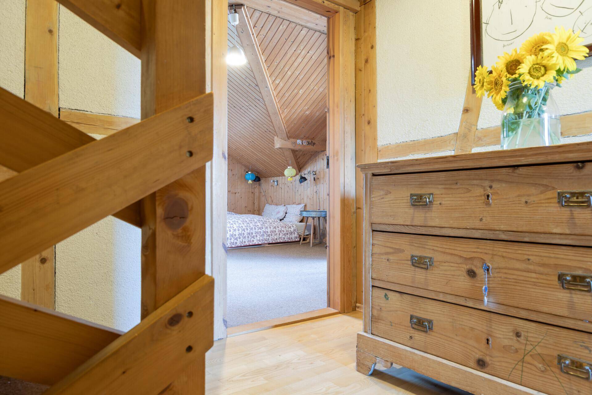 Heller Flur mit Holztreppe und Kommode, der zu einem Schlafzimmer im Dachgeschoss führt.
