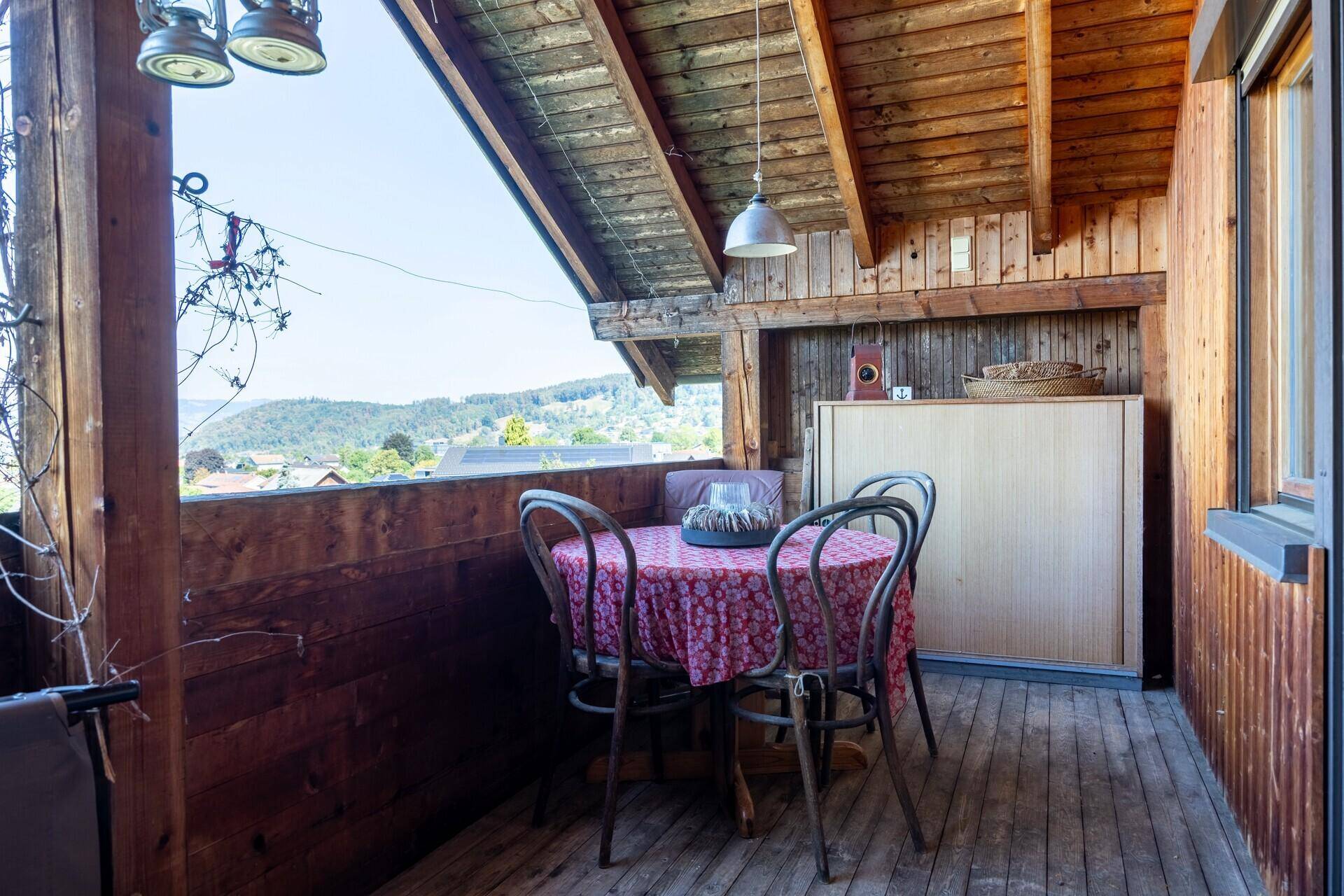 Gemütlicher Balkon mit Esstisch und Stühlen, umgeben von Holzverkleidung und mit Ausblick.