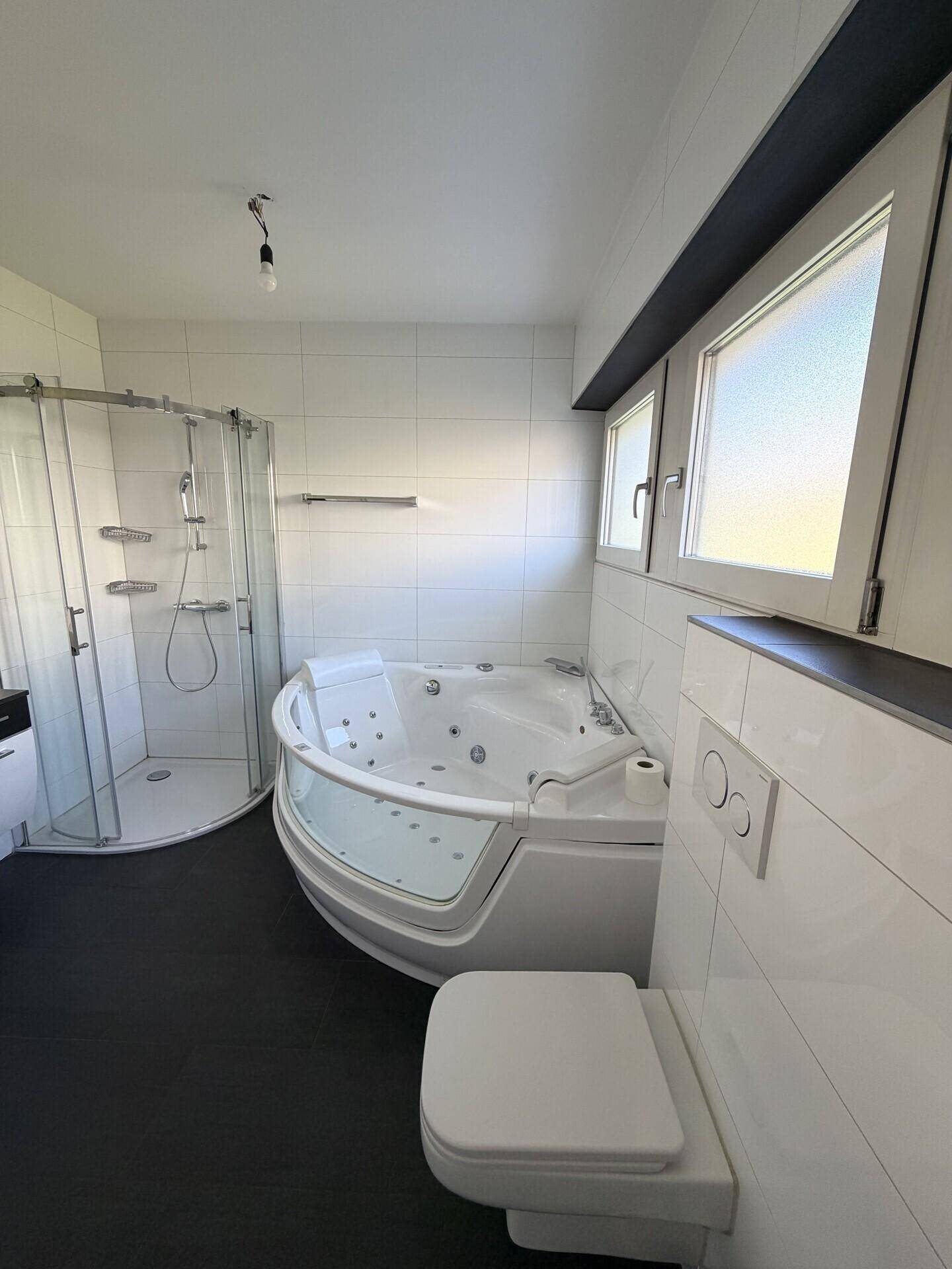 Helles Badezimmer mit Whirlpool, Duschkabine und Fenster für Tageslicht.