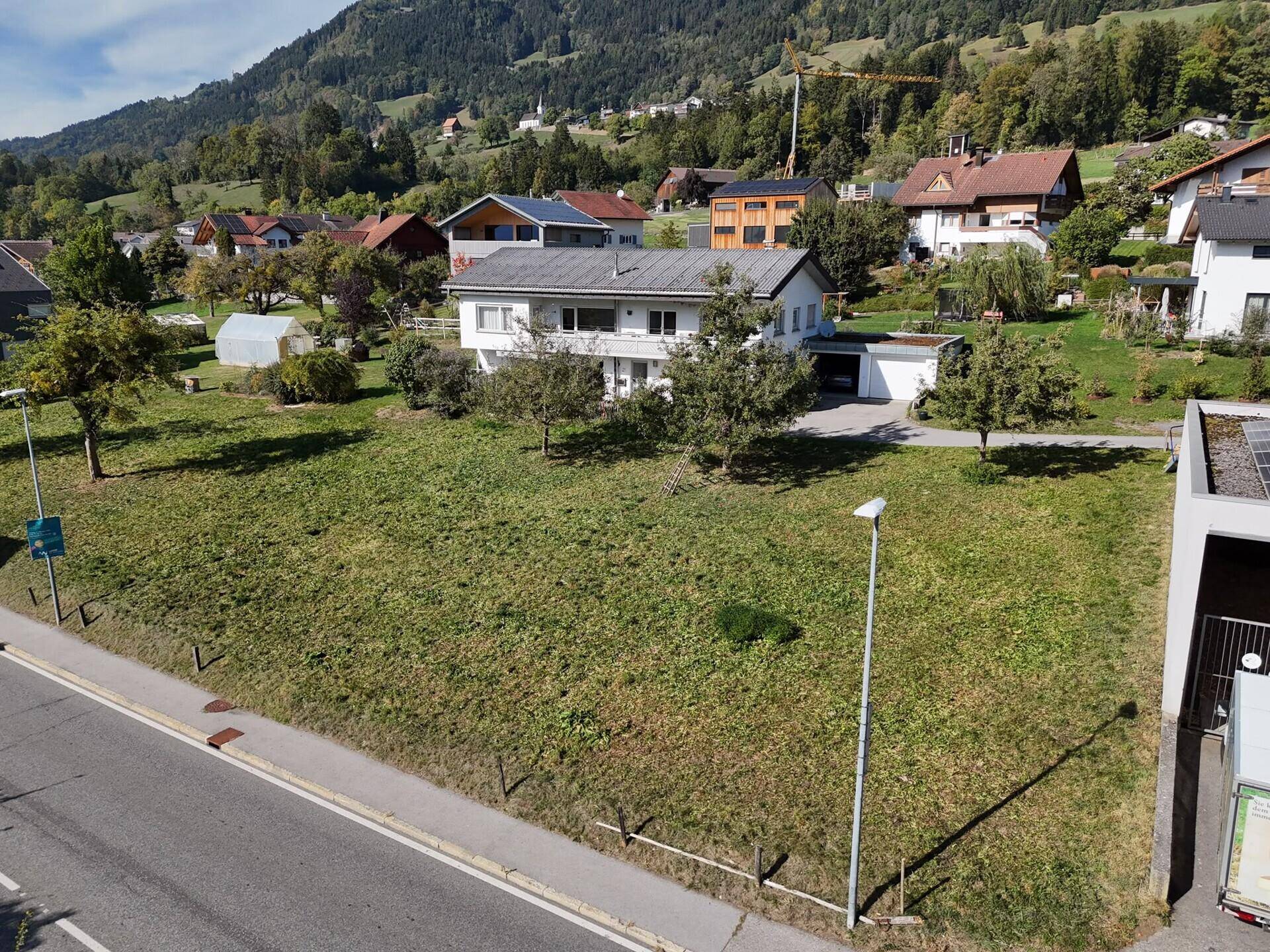 Übersicht des Grundstücks mit angrenzender Straße, umliegenden Häusern und bewaldeten Hügeln.
