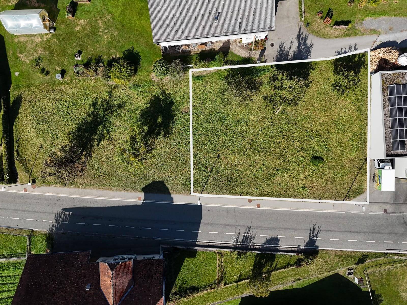 Luftaufnahme eines Grundstücks, weiß umrandet, mit angrenzender Straße und umliegenden Gebäuden.