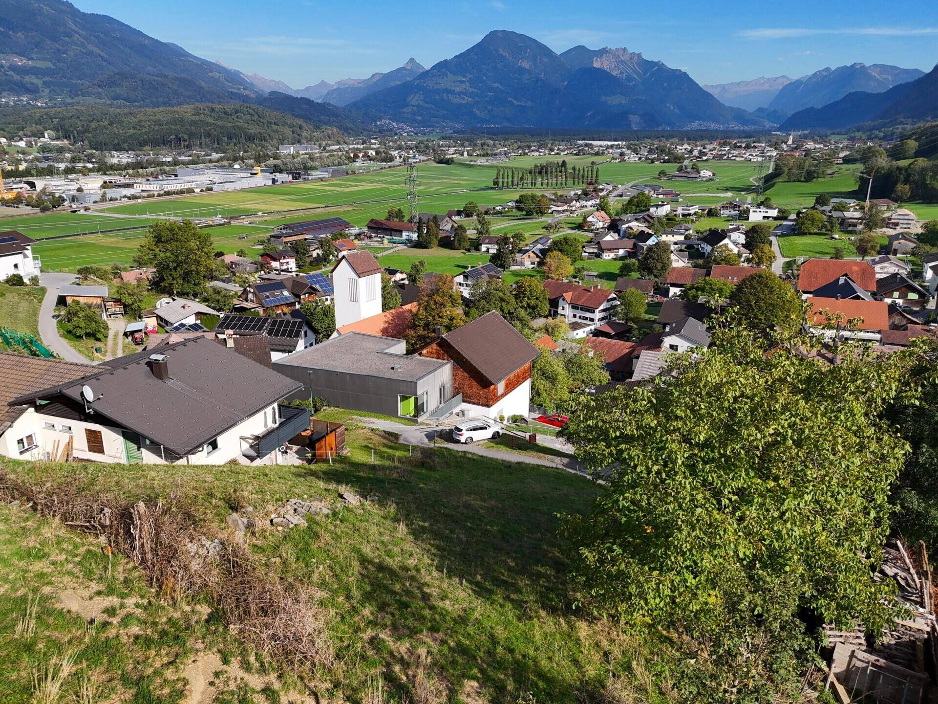 Blick von oben auf eine Wohnsiedlung am Hang, umgeben von Natur und mit Bergsicht.
