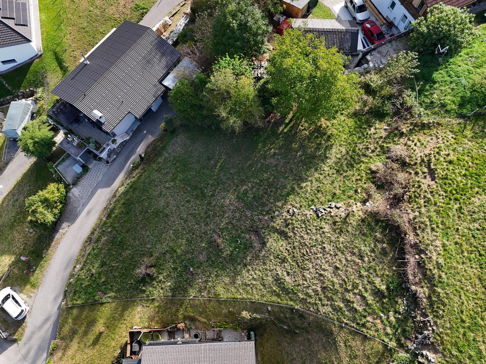 Luftaufnahme eines unbebauten Grundstücks mit angrenzenden Häusern und Zufahrtsweg.