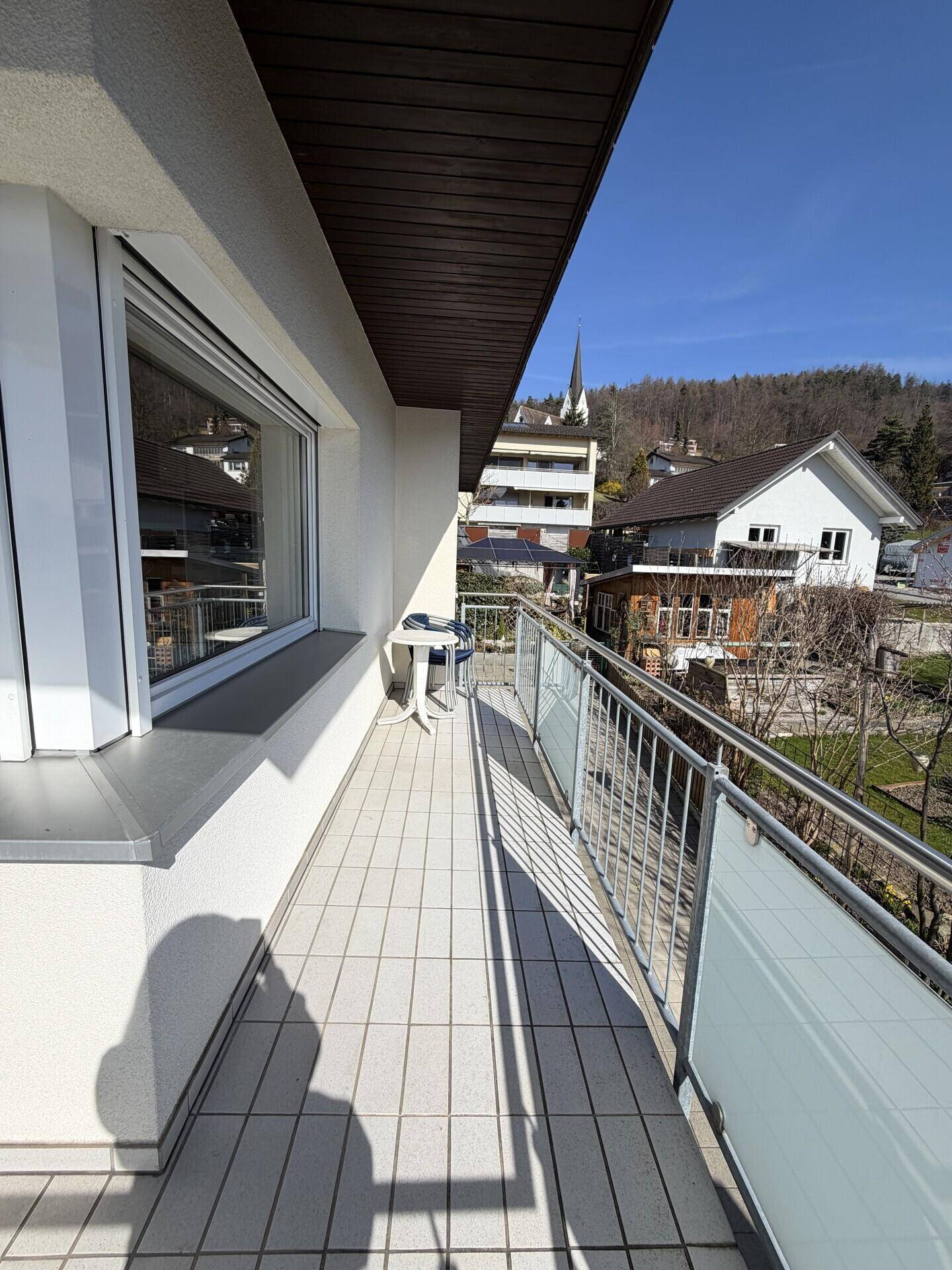 Langer Balkon mit Fliesenboden, Metallgeländer und Markise für Schatten.