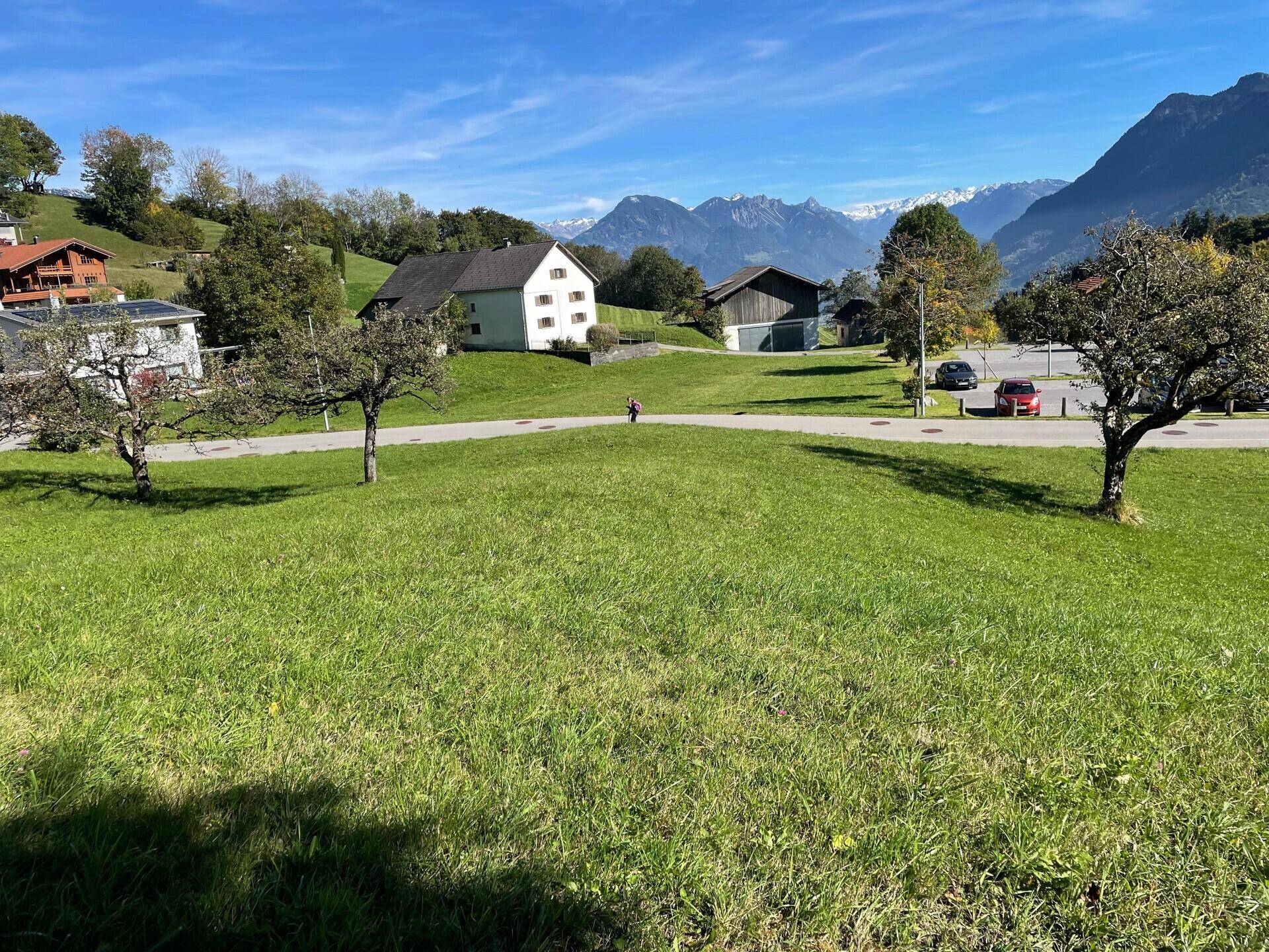 Weitläufiges grünes Grundstück mit Panoramablick auf die Berge und umliegende Bebauung an einem sonnigen Tag.
