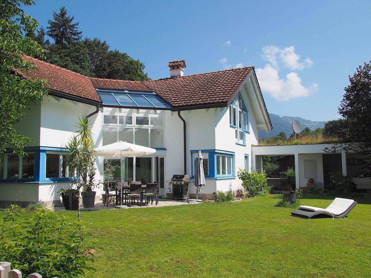 Sonniger Außenbereich mit Terrasse, Gartenmöbeln und weitem Blick auf die umliegende Natur und Berge.