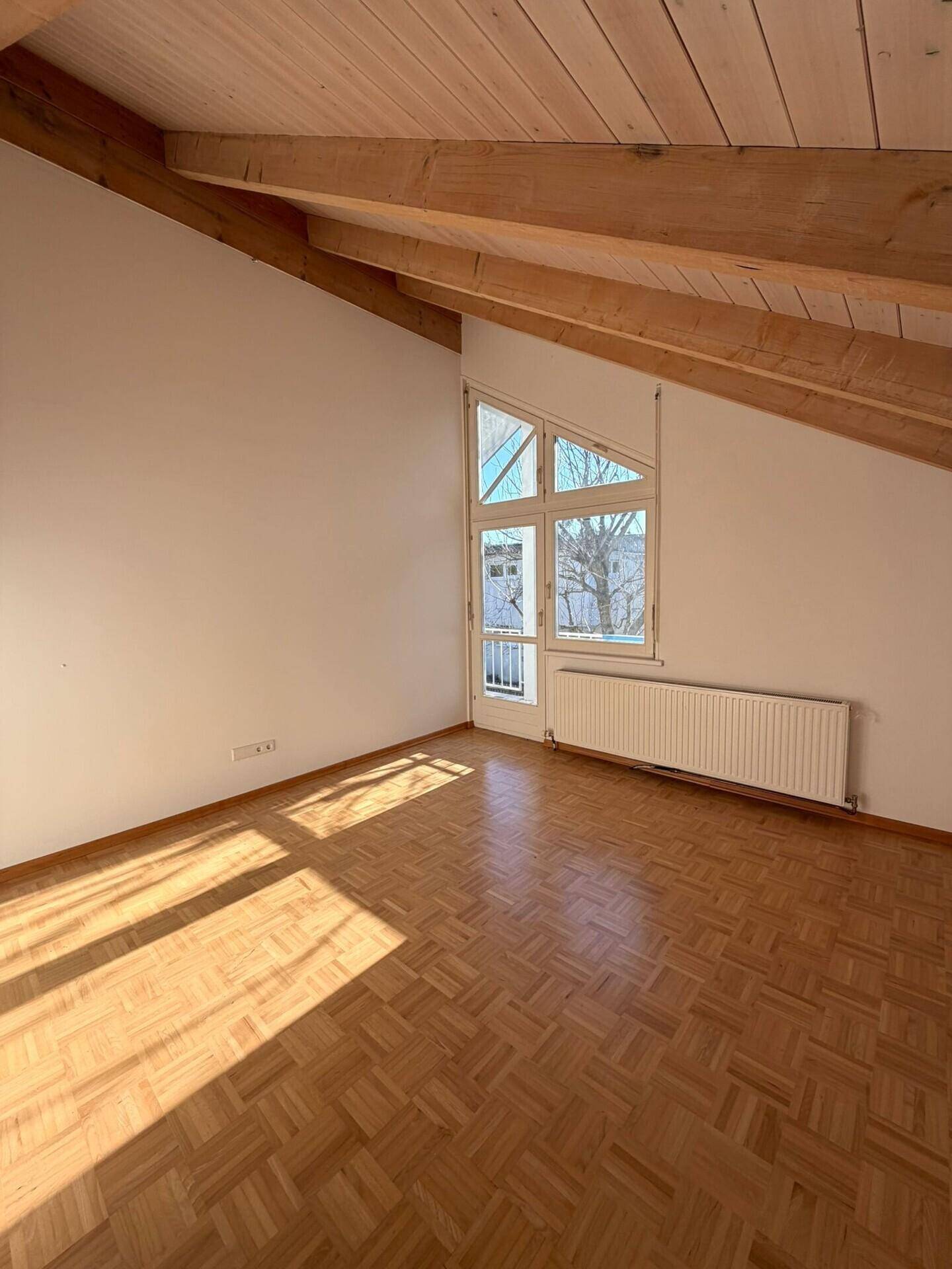 Lichtdurchfluteter Raum mit Parkettboden und Holzdecken, ideal als Schlaf- oder Arbeitszimmer.