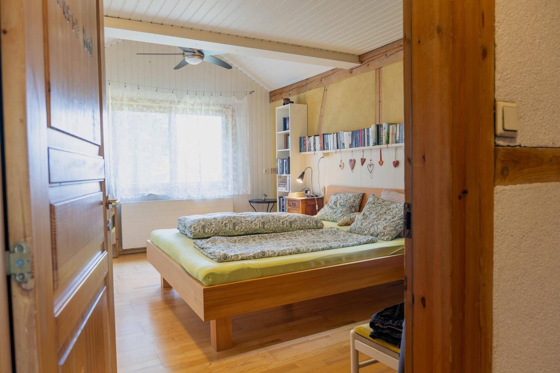 Helles Schlafzimmer mit Holzboden, Deckenventilator und großem Fenster für viel Tageslicht.