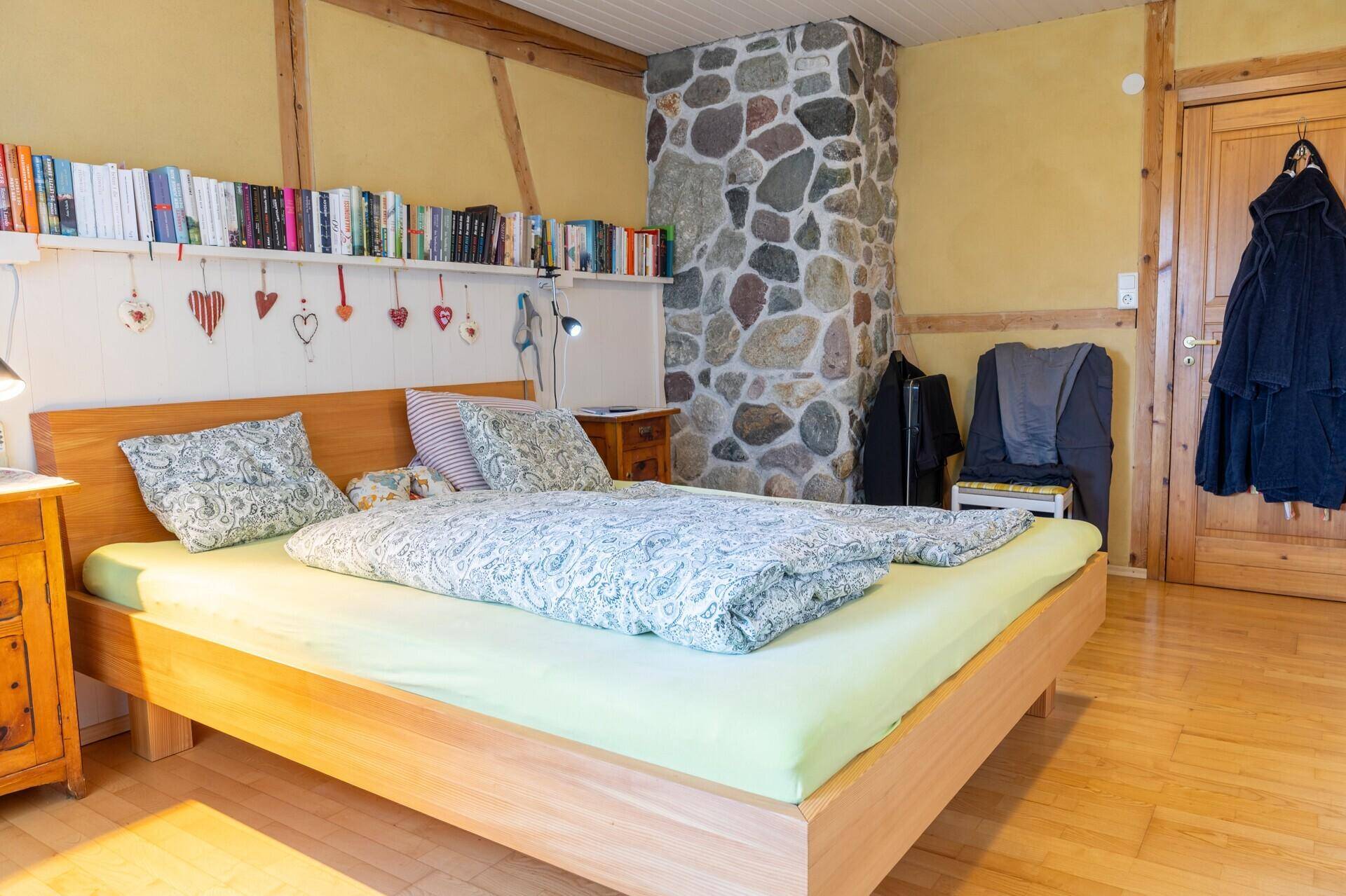 Schlafzimmer mit rustikalem Steinsäulen-Detail, Holzboden und Bücherregal über dem Bett.
