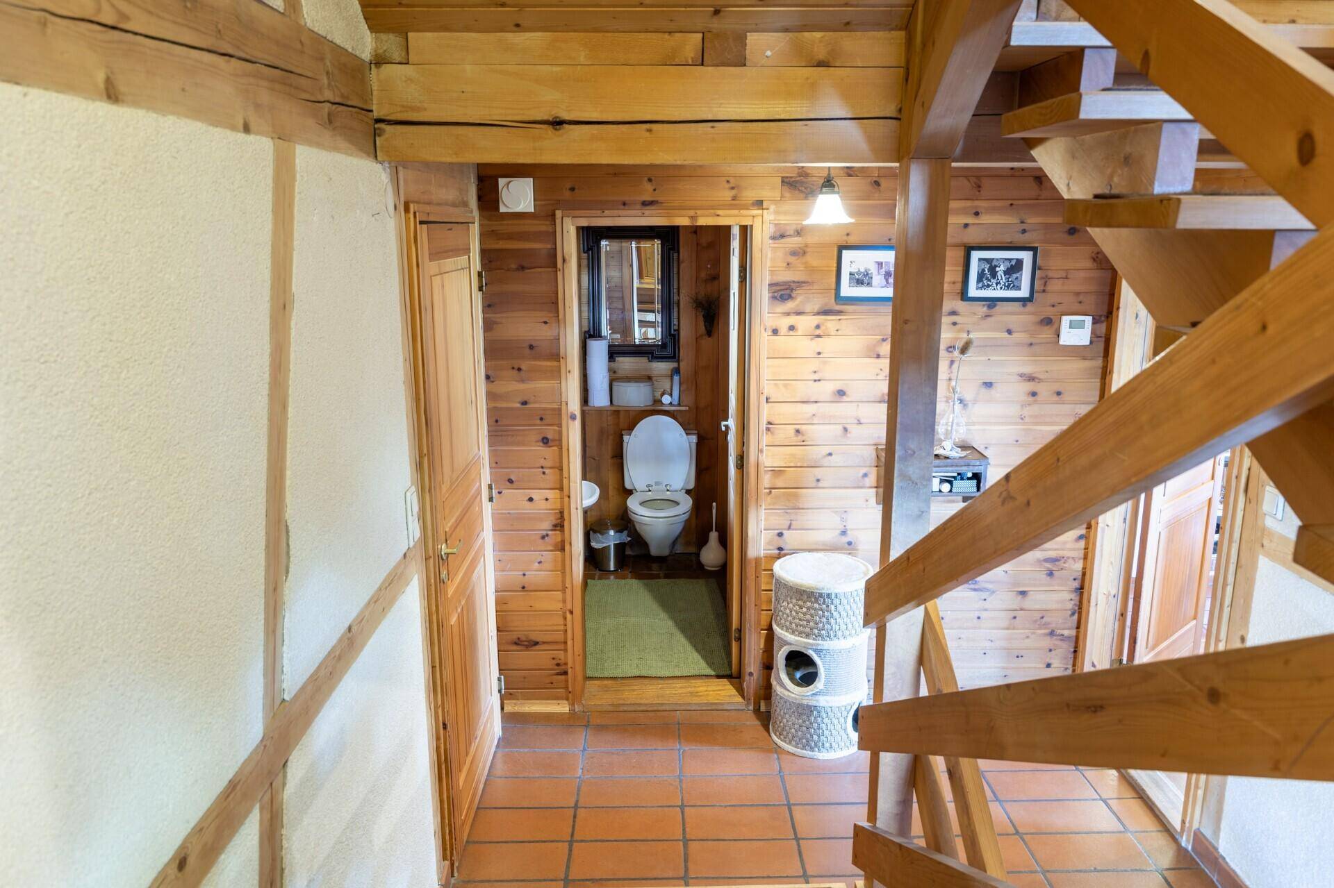 Flur mit Holzverkleidung und Terracotta-Boden, der zu einer separaten Toilette führt.