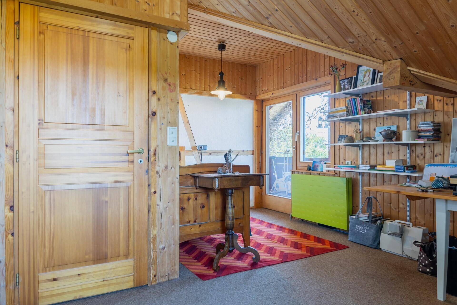 Heller Raum mit Holztüren, Schreibtisch und Zugang zu einem Balkon, umgeben von Holzverkleidung.
