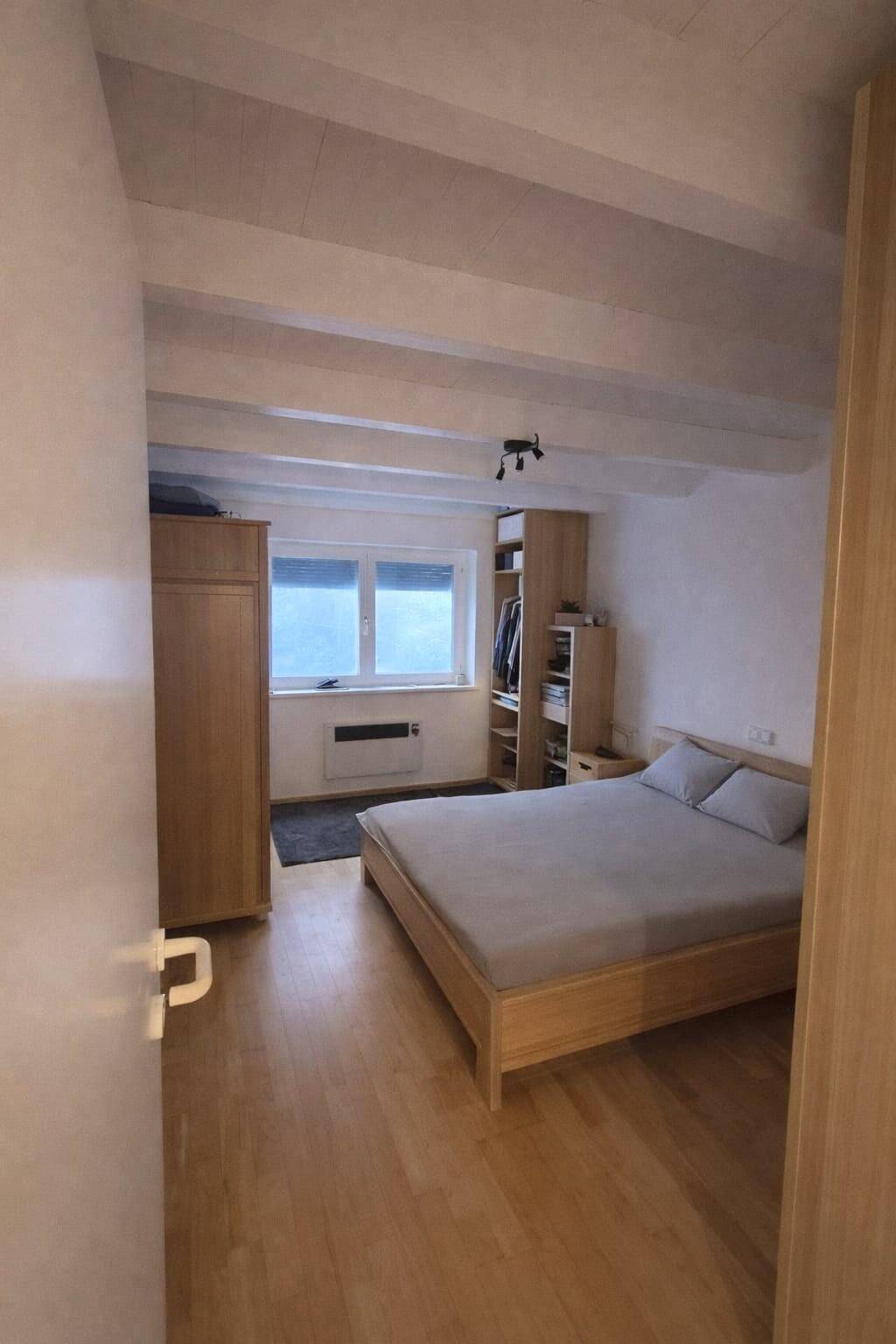 Schlafzimmer mit Holzbett, Einbauschränken und Holzboden, unter sichtbaren Deckenbalken.