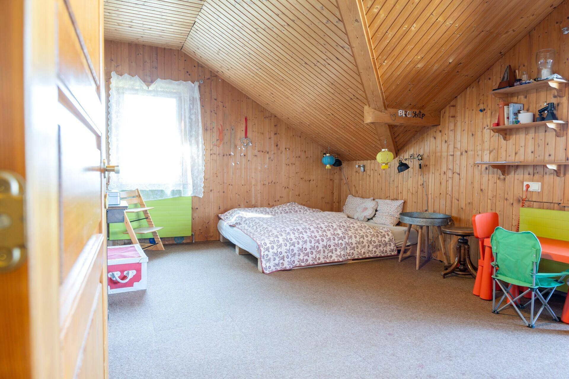 Gemütliches Schlafzimmer im Dachgeschoss mit Holzverkleidung, schrägen Decken und Fenster.
