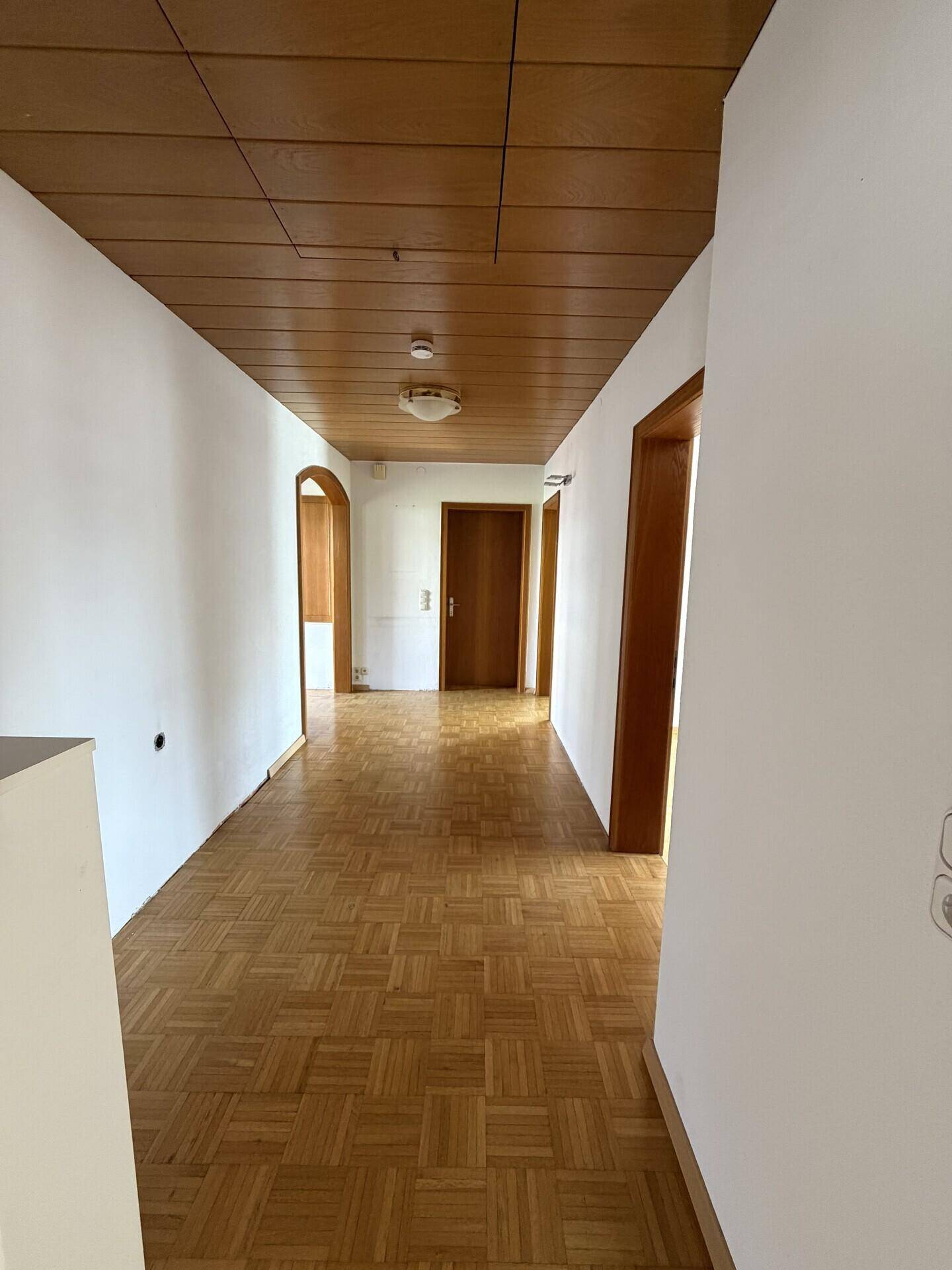 Heller Flur mit Parkettboden und Holzdecke, der zu weiteren Räumen führt.