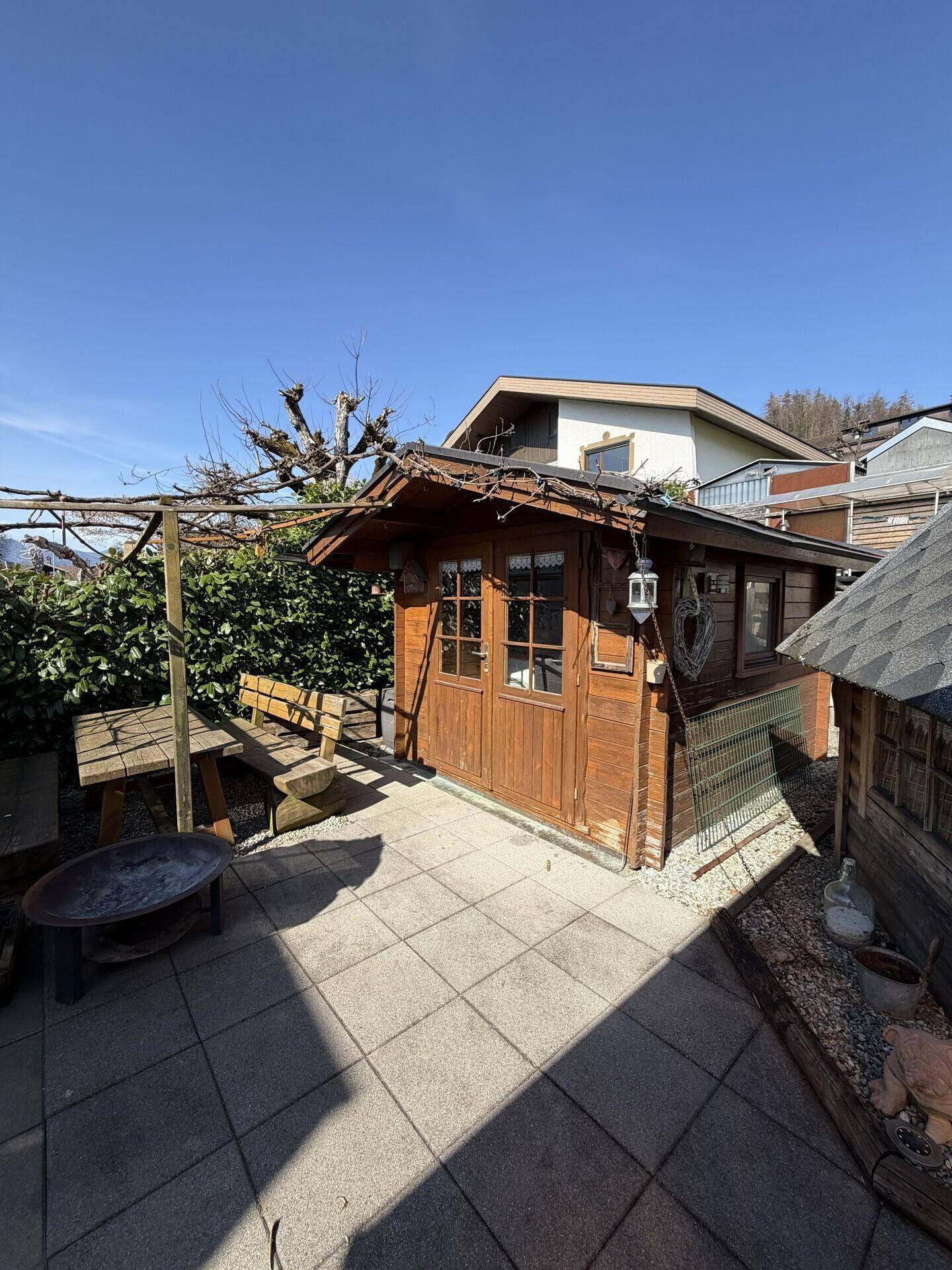 Gemütlicher Terrassenbereich mit Holzgartenhaus, Sitzgelegenheiten und Feuerstelle.