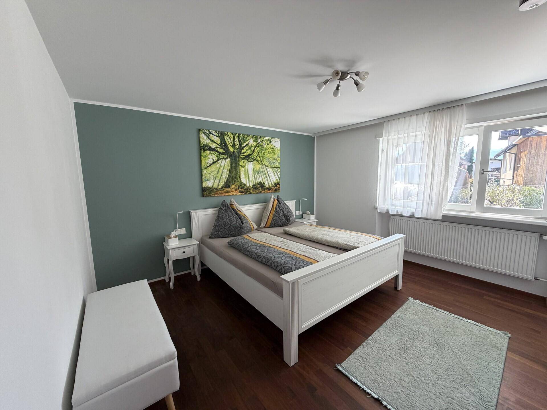 Schlafzimmer mit Doppelbett, Holzboden und Fenster mit Blick auf die Umgebung.