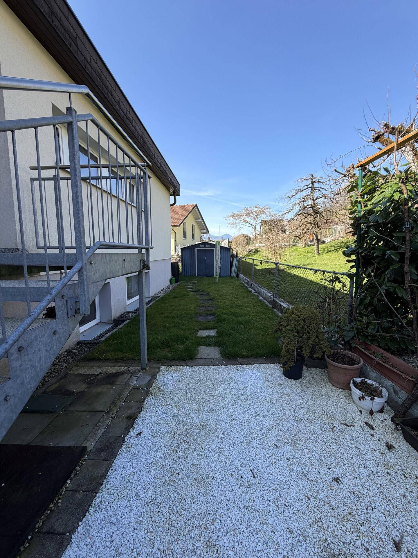 Kleiner Gartenbereich mit Rasenfläche, Gartenhaus und Treppenzugang.