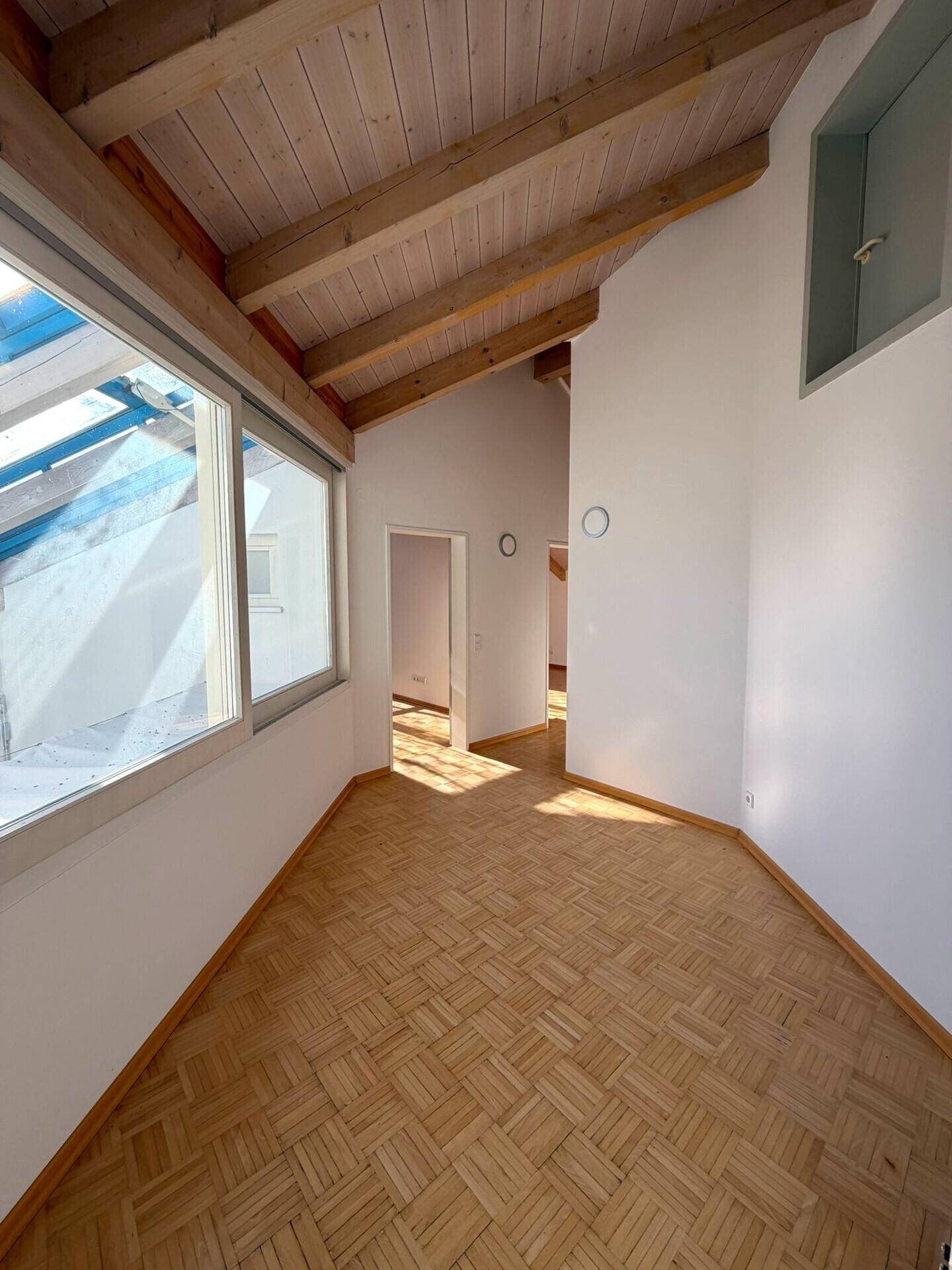 Heller Flur mit Parkettboden und sichtbaren Deckenbalken, führt zu weiteren Räumen.