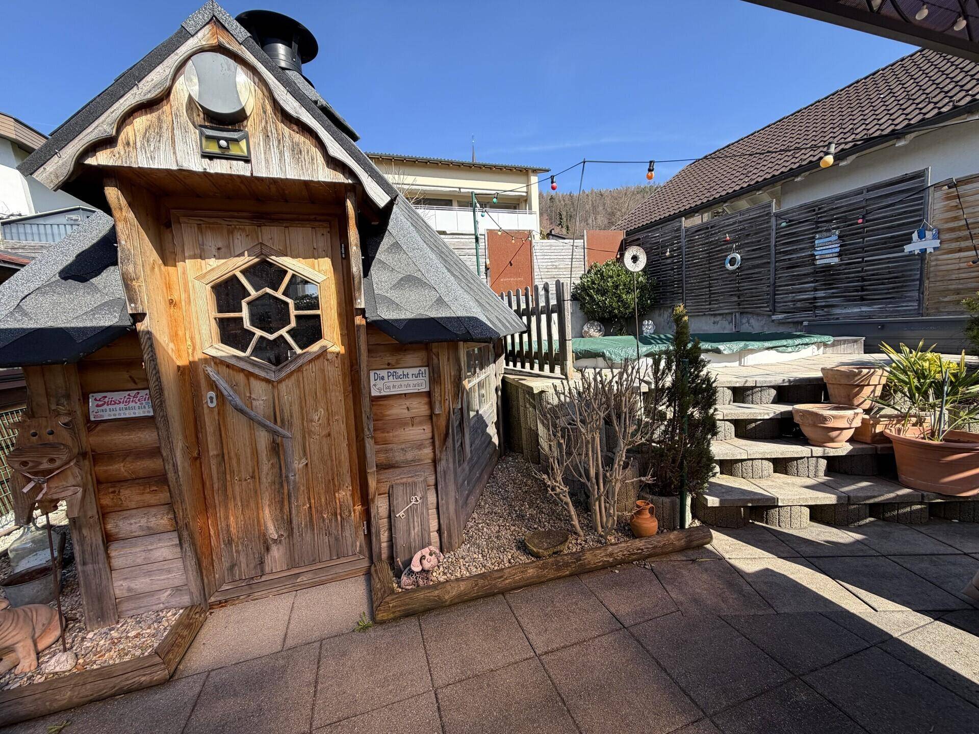 Gepflasterter Terrassenbereich mit dekorativem Holzhaus und Stufen.