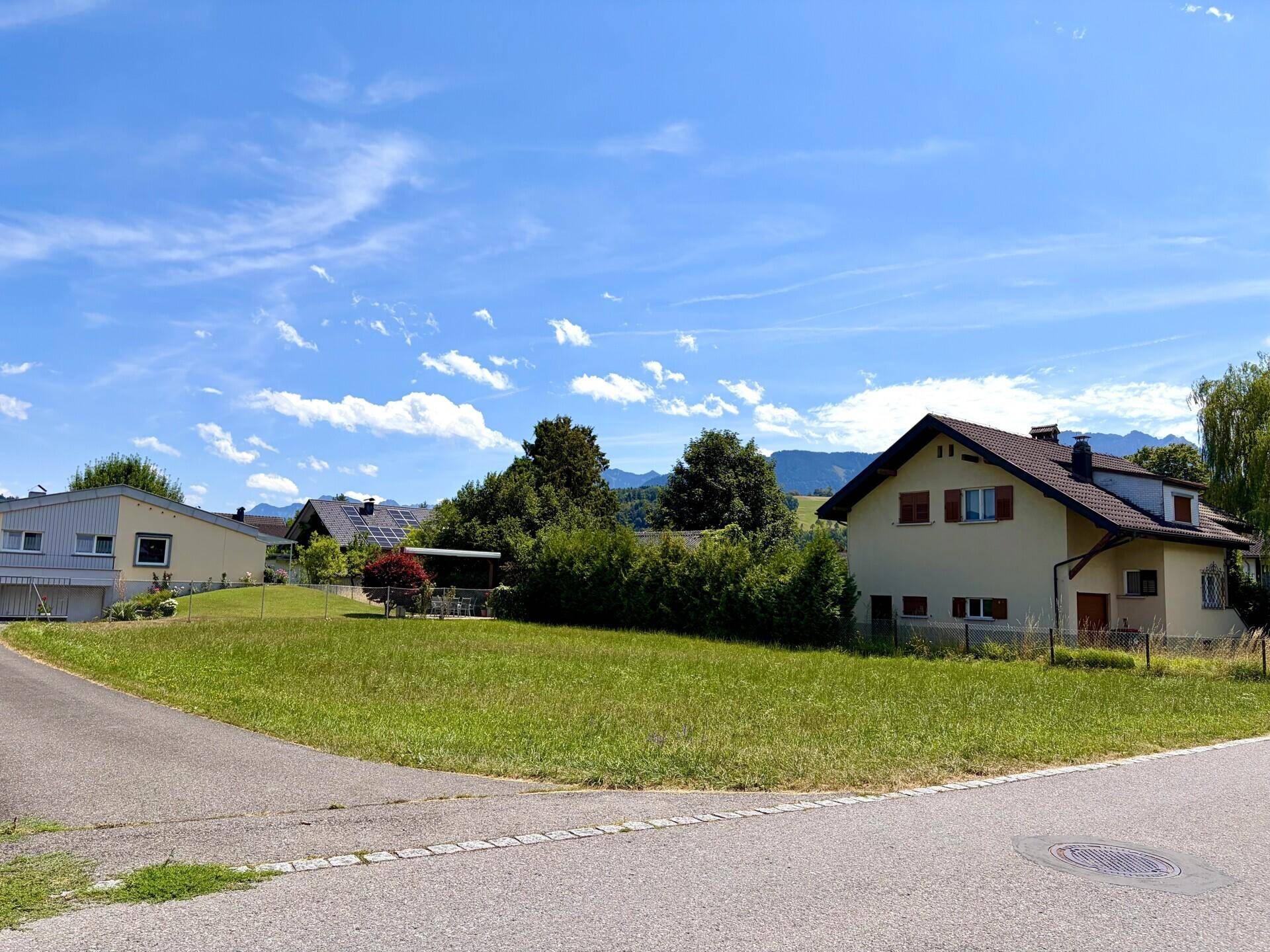 Grünes Baugrundstück in ländlicher Umgebung mit Blick auf die umliegenden Berge und Häuser.