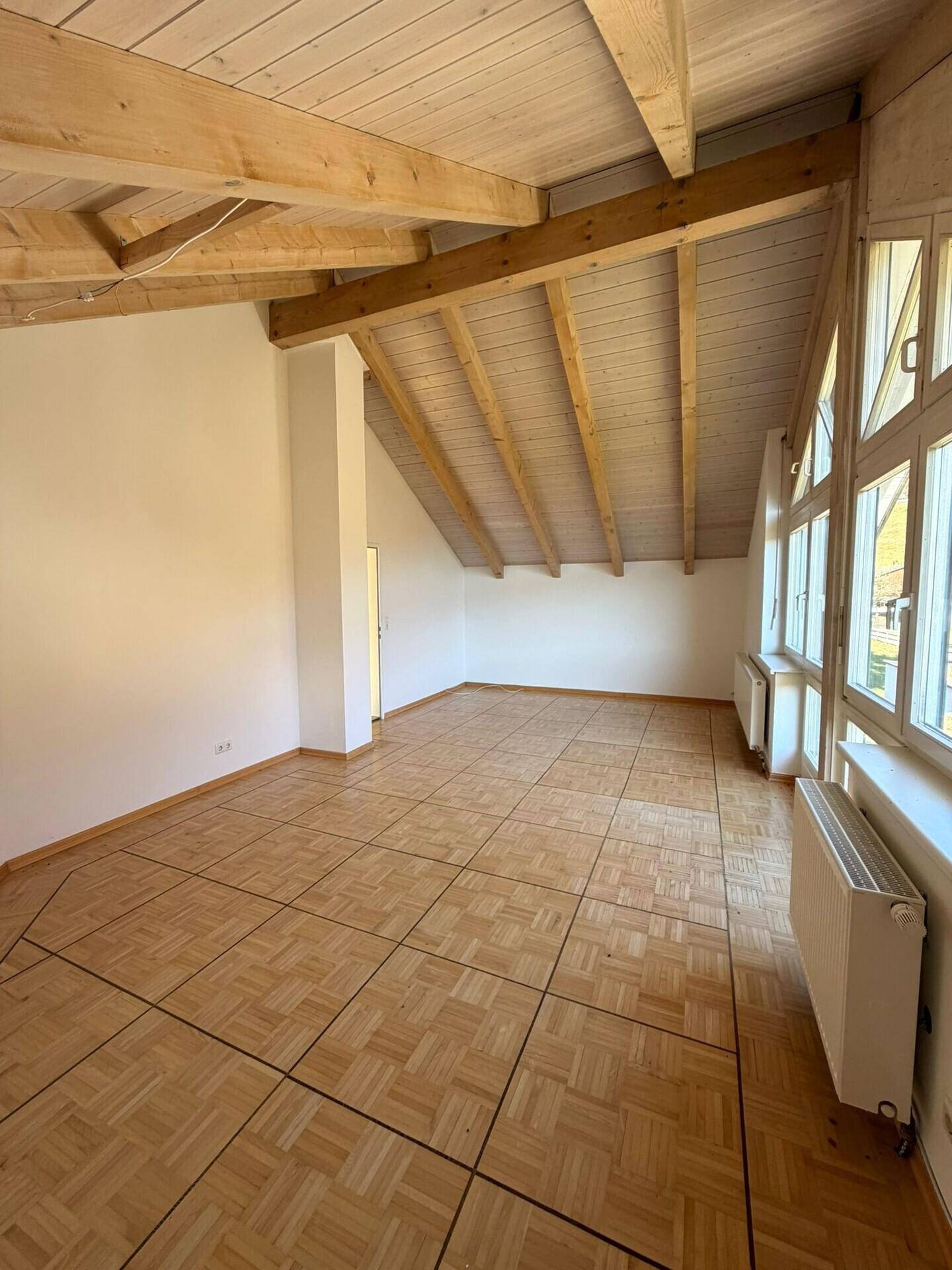 Heller Wohnbereich mit Parkettboden und schrägen Holzdecken, bietet viel natürliches Licht durch große Fenster.