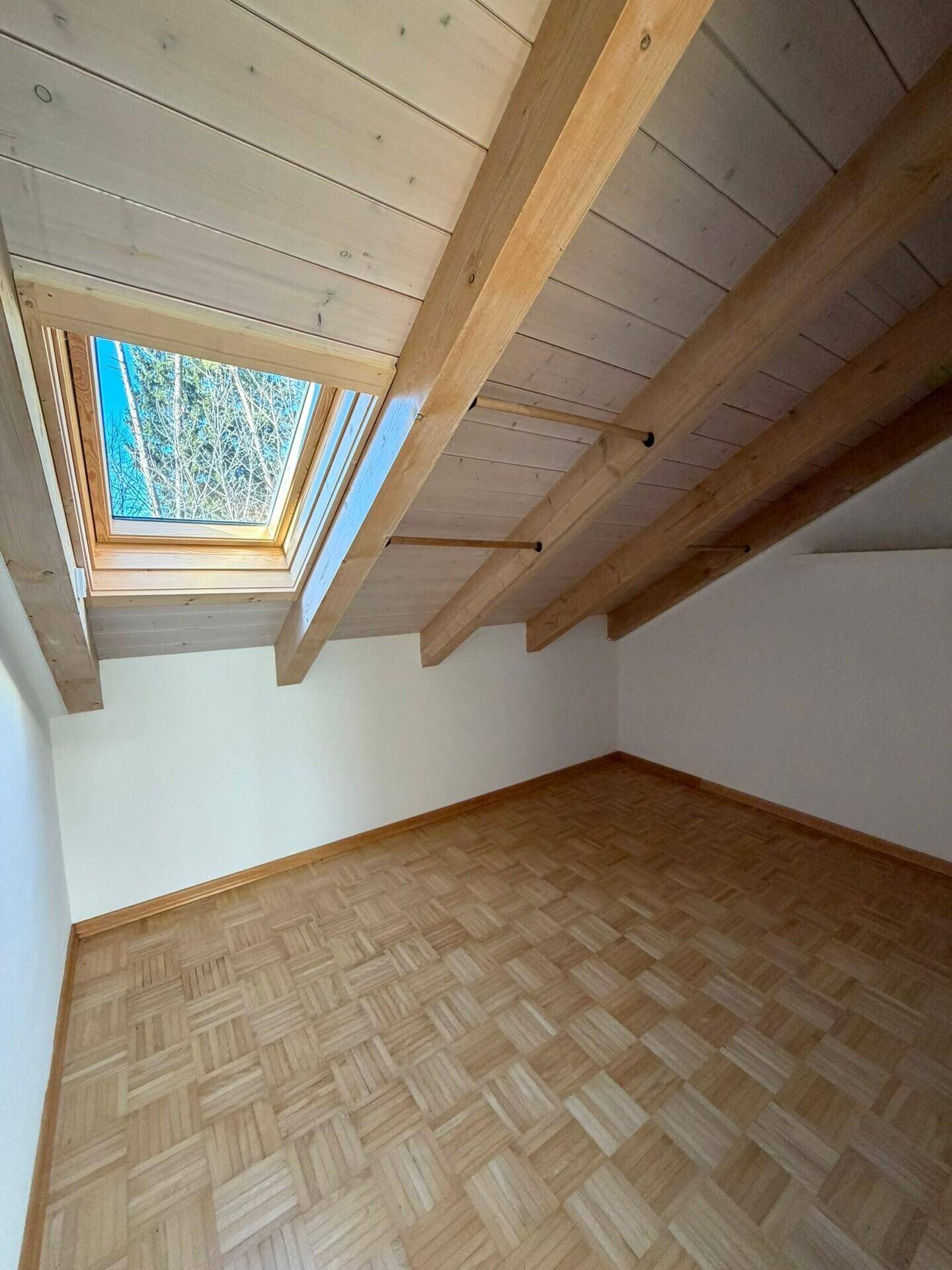Kleinerer Raum mit Parkettboden, Holzdecke und Dachfenster, bietet zusätzliches Tageslicht.