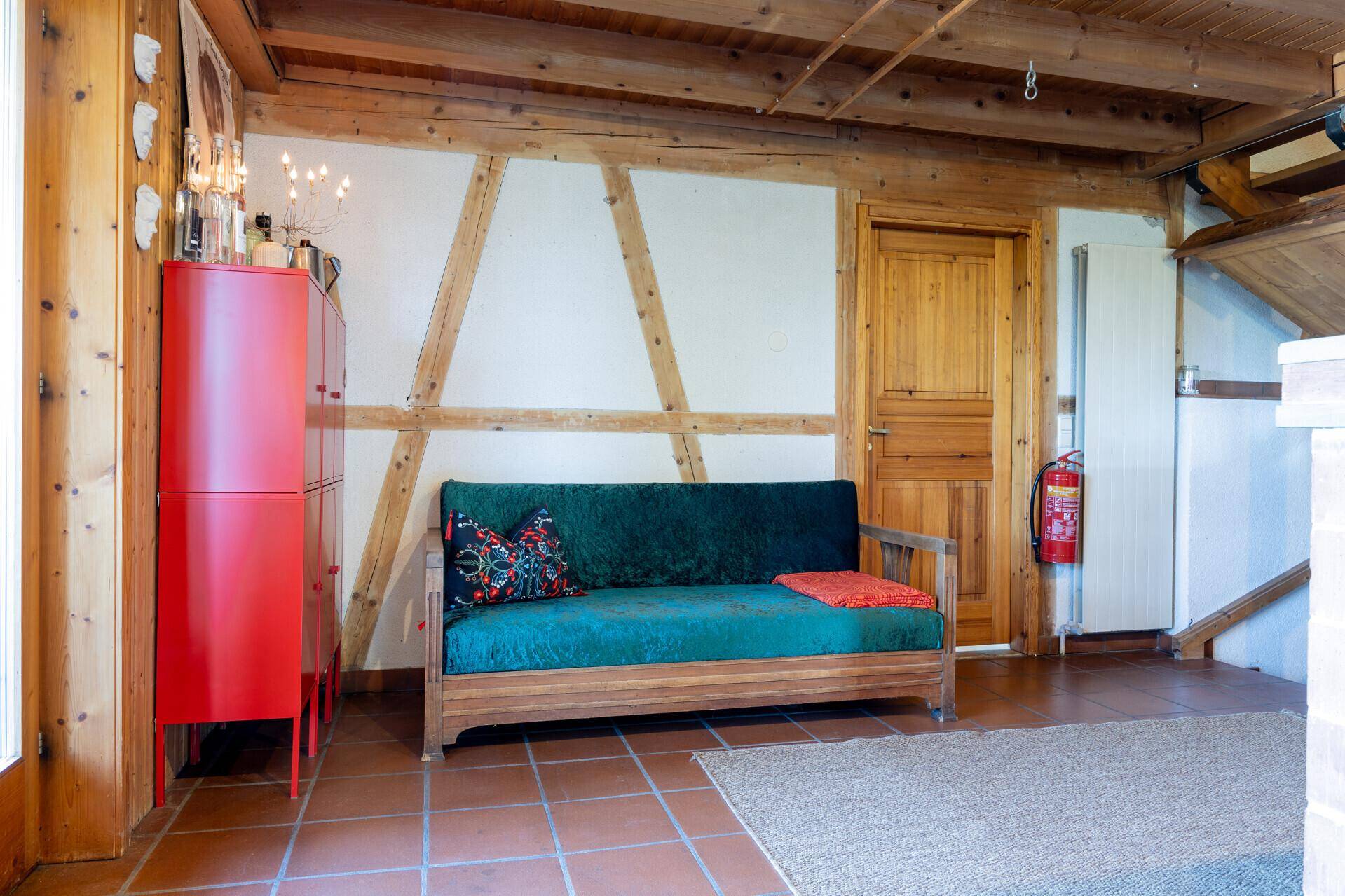 Rustikales Wohnzimmer mit sichtbaren Holzbalken, Terrakottafliesen und einem farbenfrohen roten Schrank.
