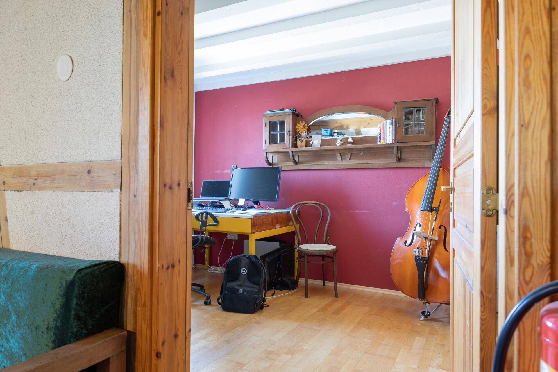 Arbeitszimmer mit Holzboden, roter Wand und einem Kontrabass, ideal für kreative Tätigkeiten.