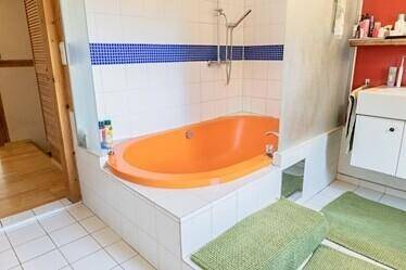Nahaufnahme der orangefarbenen Badewanne mit Duschfunktion und blauen Akzentfliesen.