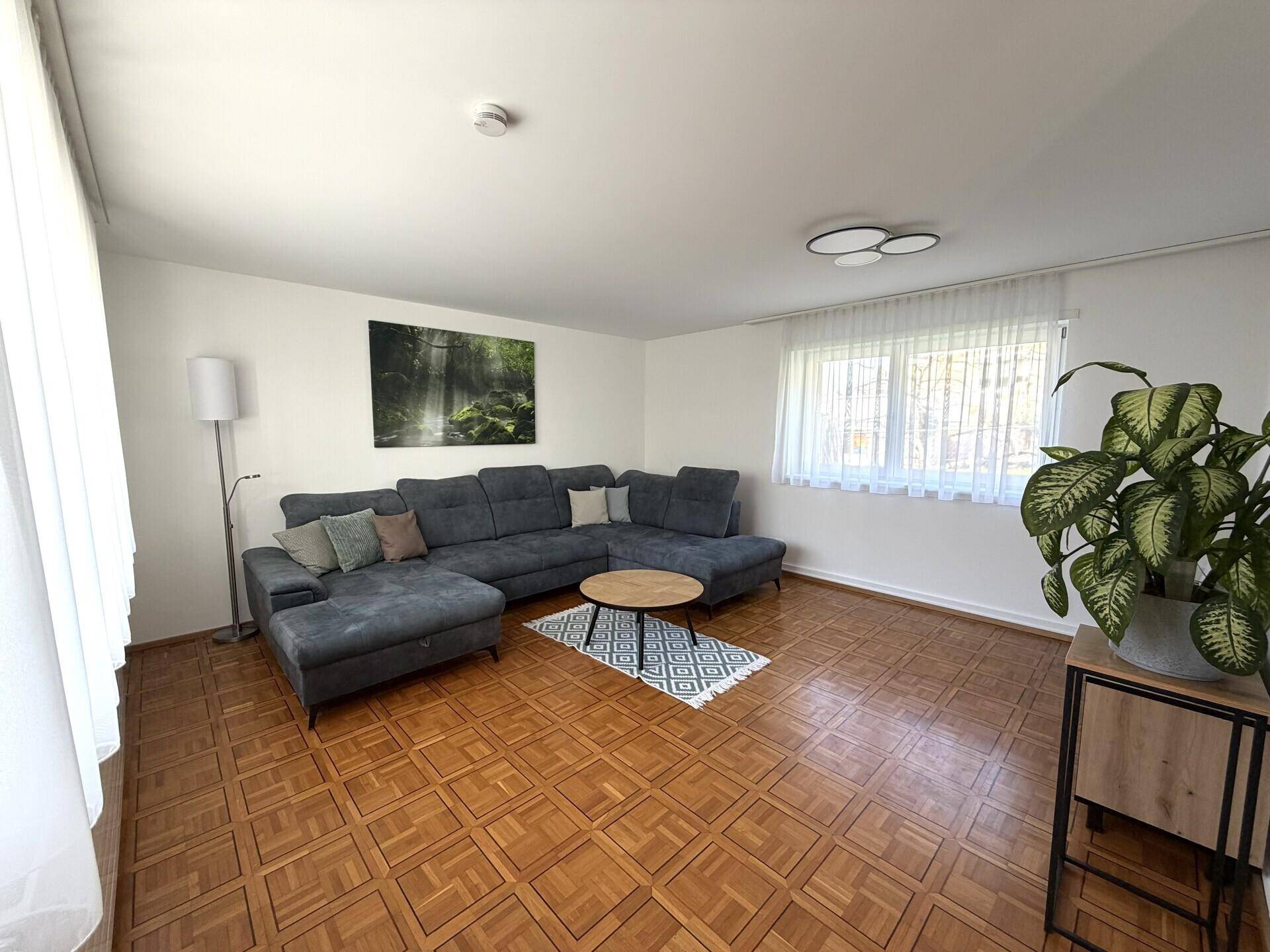 Helles Wohnzimmer mit großem Ecksofa, Parkettboden und Blick ins Grüne.