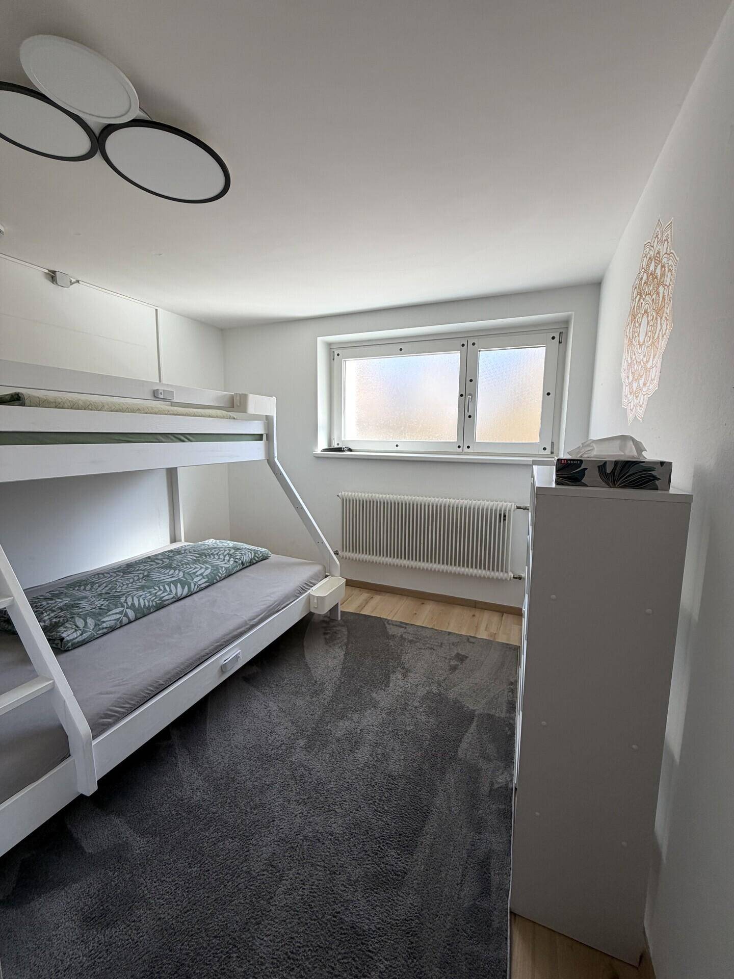 Kinderzimmer mit Etagenbett, Teppichboden und hellem Fenster.