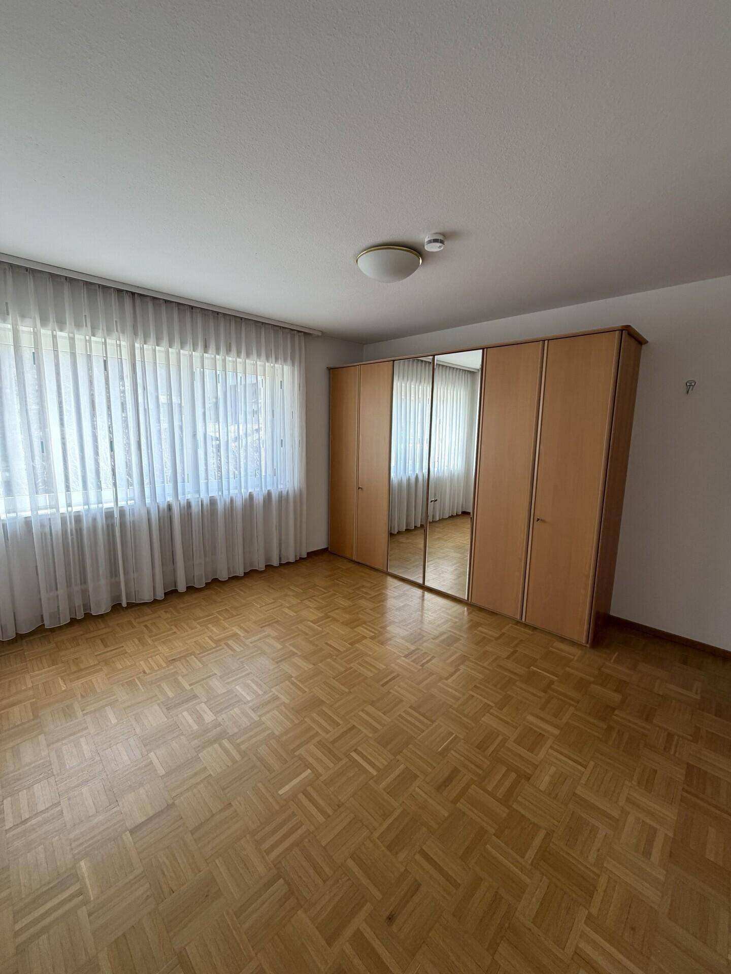 Helles Schlafzimmer mit Parkettboden und großem Spiegelschrank.