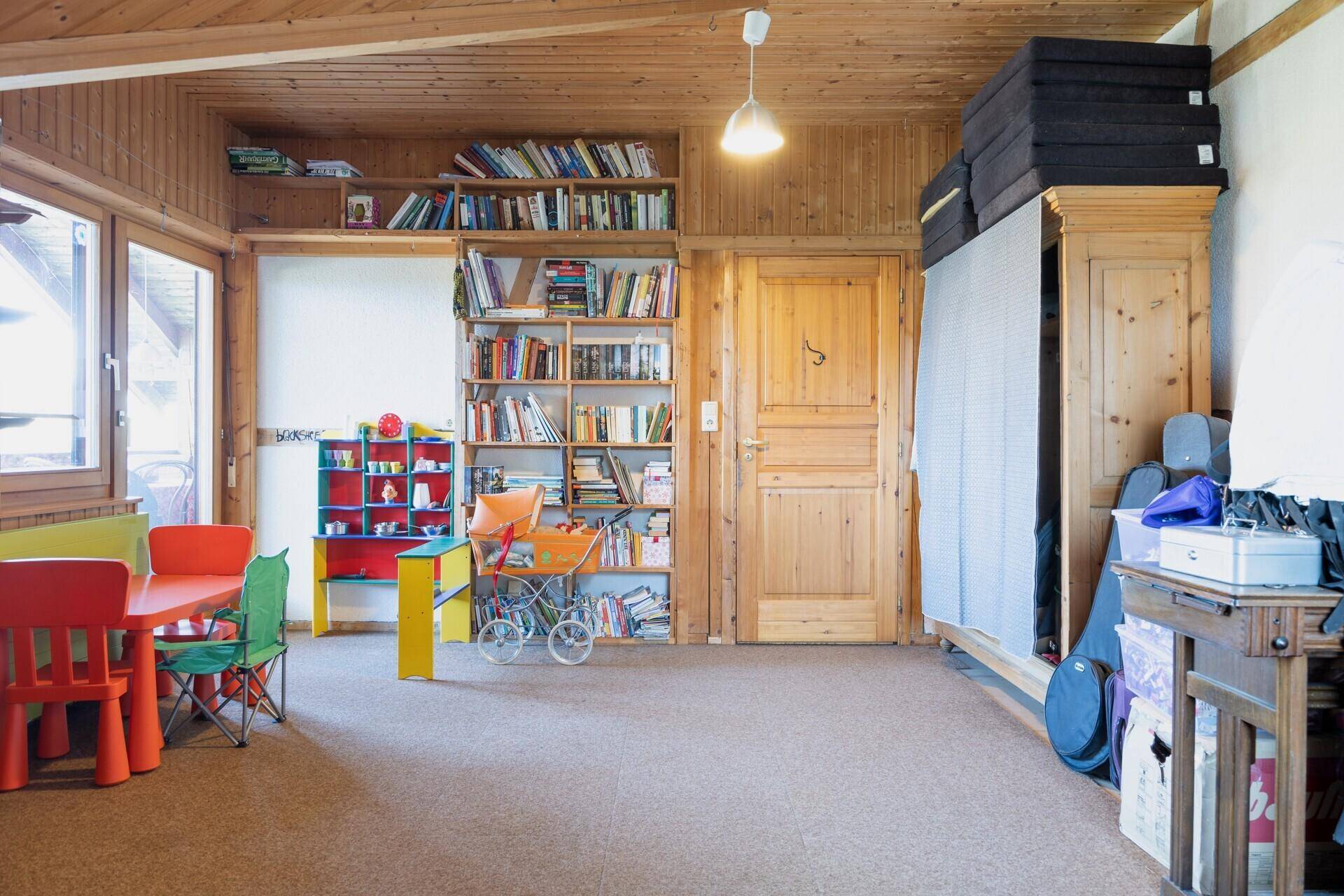 Vielseitiger Raum mit Holzverkleidung, Bücherregalen und Kindermöbeln, ideal als Spiel- oder Arbeitszimmer.