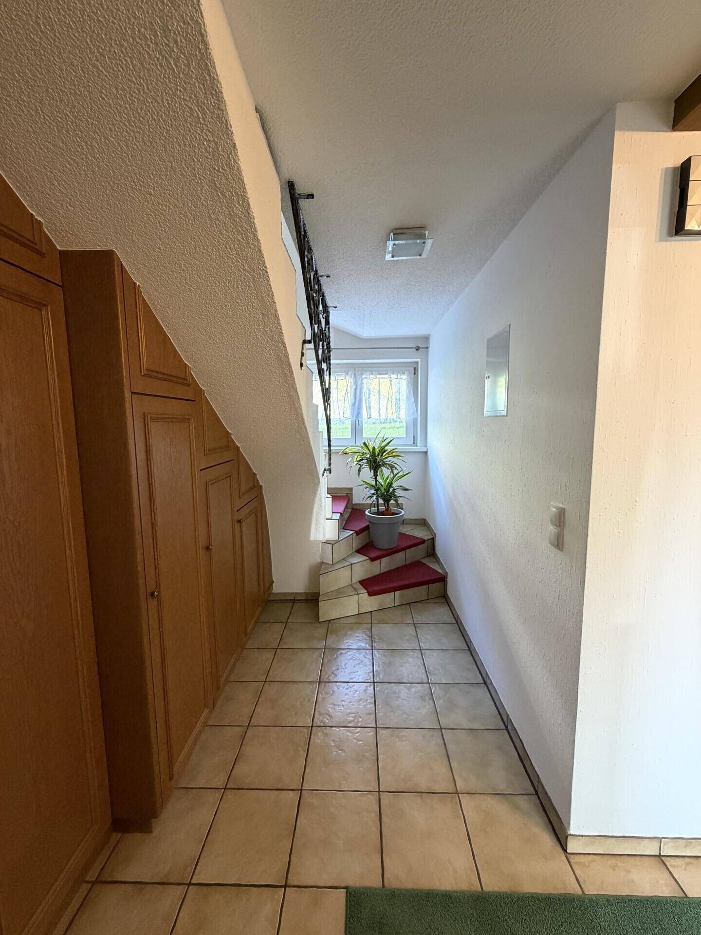 Heller Flur mit Fliesenboden und Treppenaufgang zum Obergeschoss.