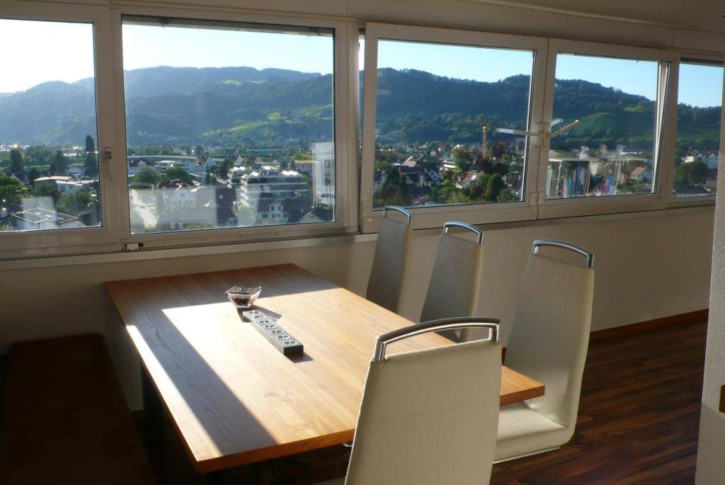 Heller Essbereich mit Holztisch und Stühlen, bietet einen weiten Blick auf die Stadt und Berge.