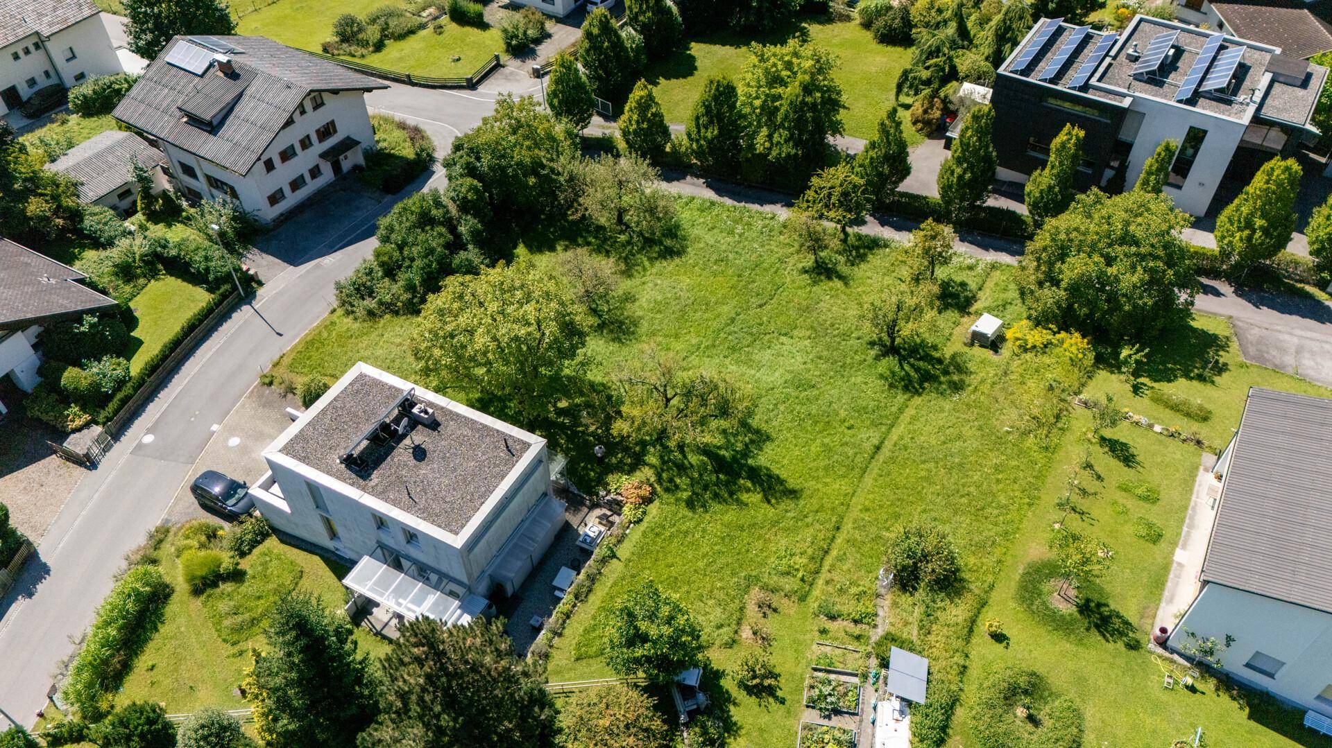 Weitläufiges grünes Baugrundstück aus der Vogelperspektive, umgeben von Wohnbebauung und viel Grün.