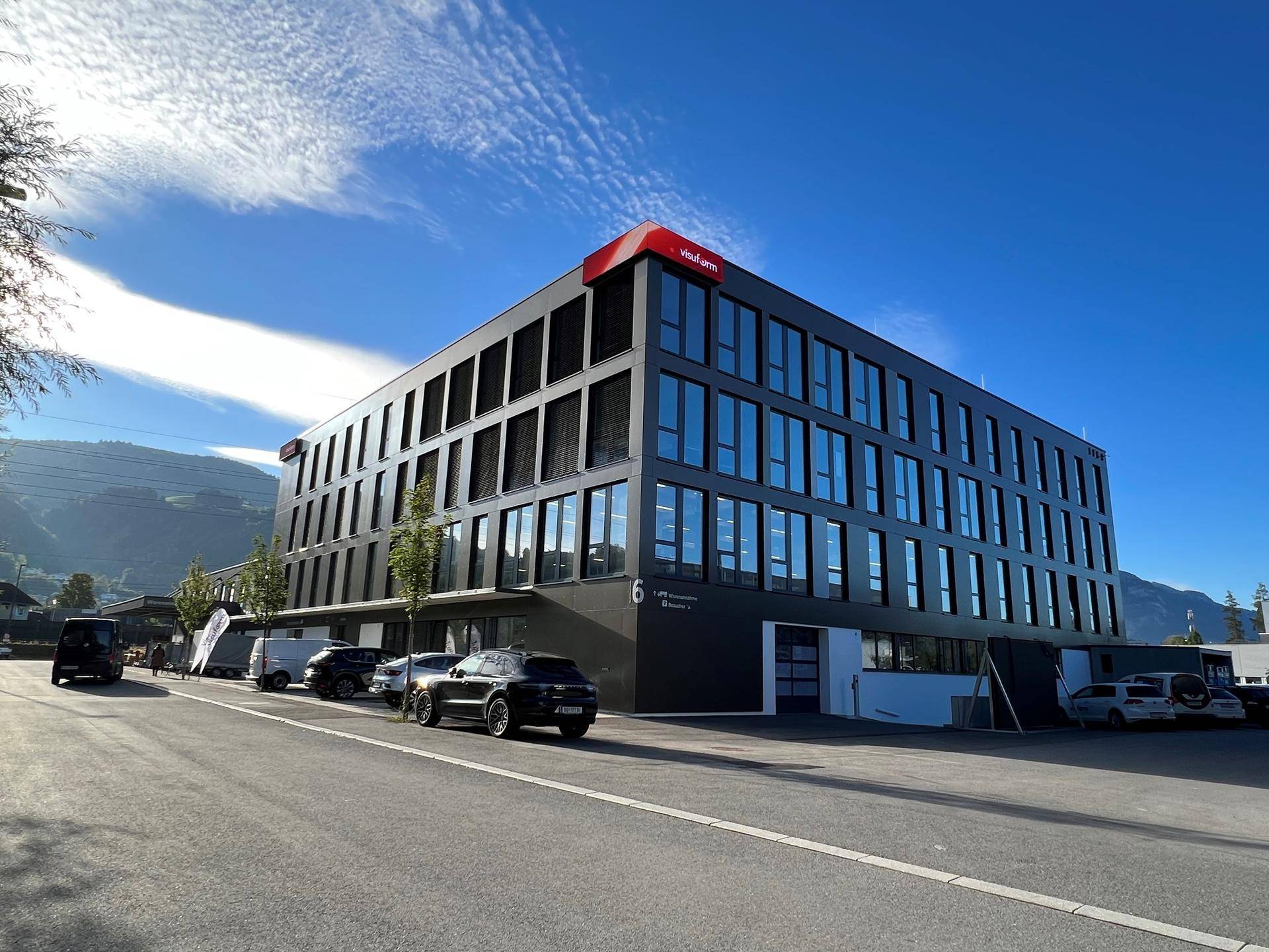 Modernes Bürogebäude mit dunkler Fassade und großen Glasflächen unter blauem Himmel.