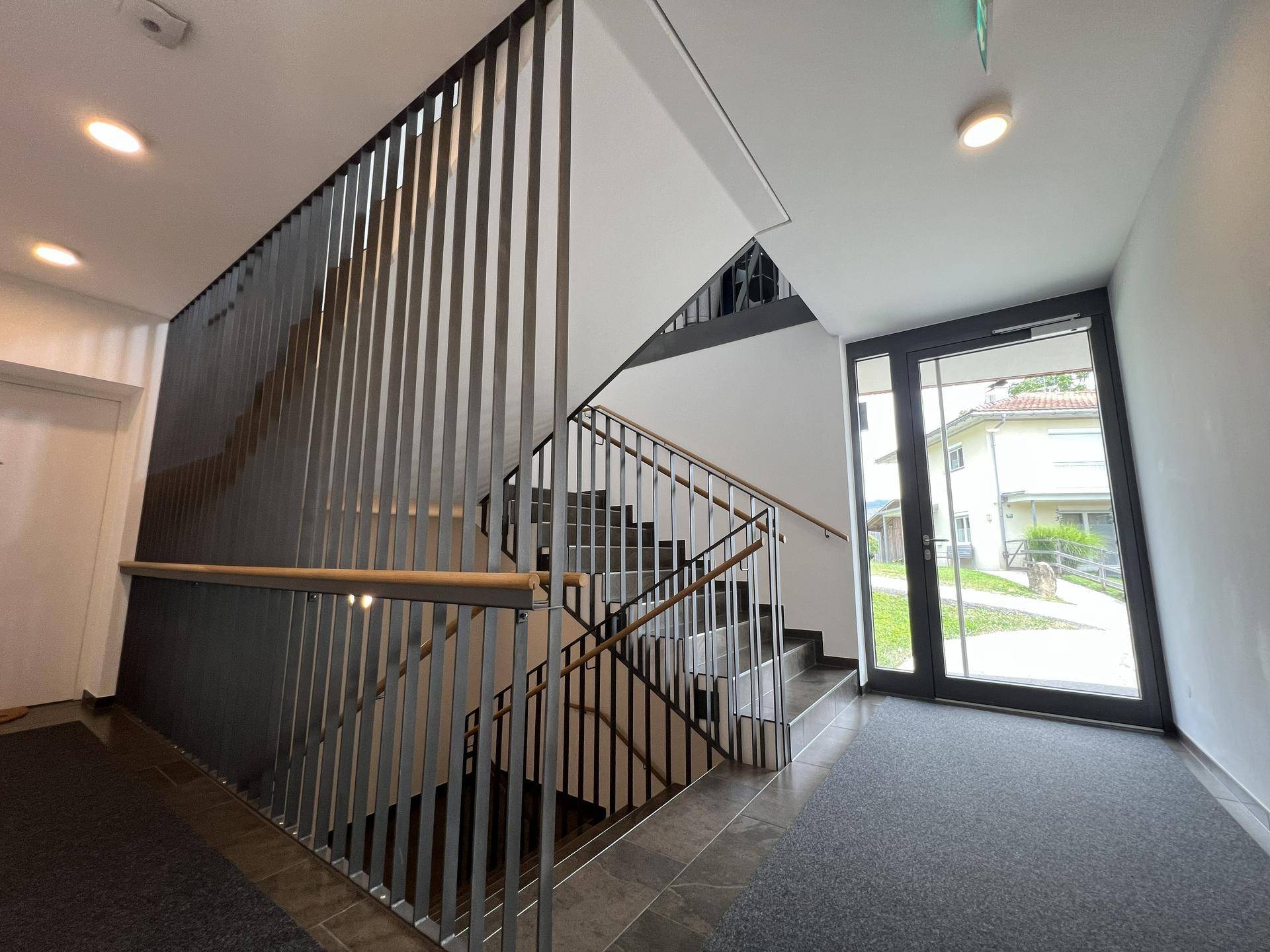 Modernes Treppenhaus mit Metallgeländer und Fliesenstufen im Eingangsbereich des Gebäudes.