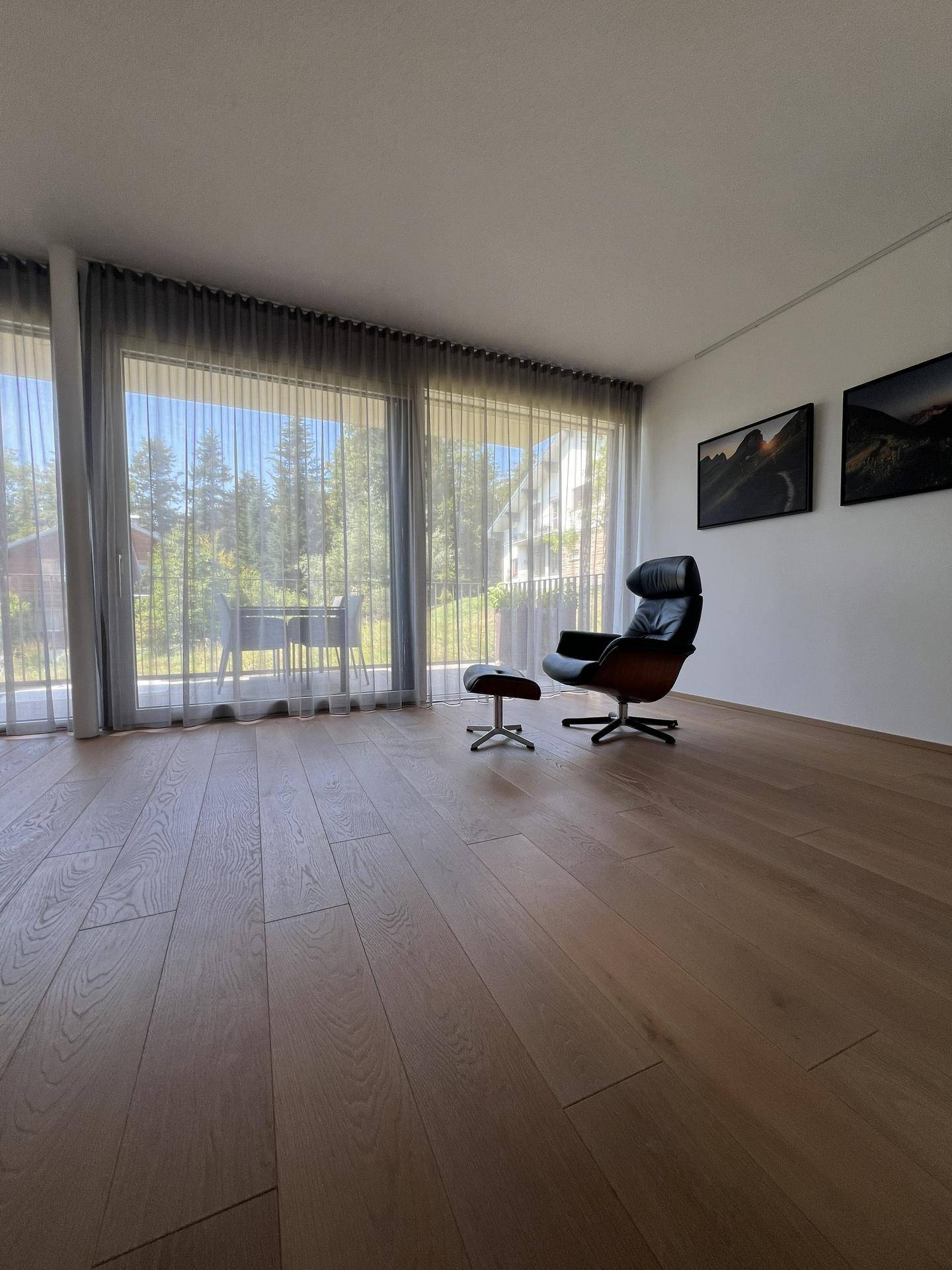 Heller Wohnbereich mit bequemem Sessel und großen Fenstern mit Blick ins Grüne.
