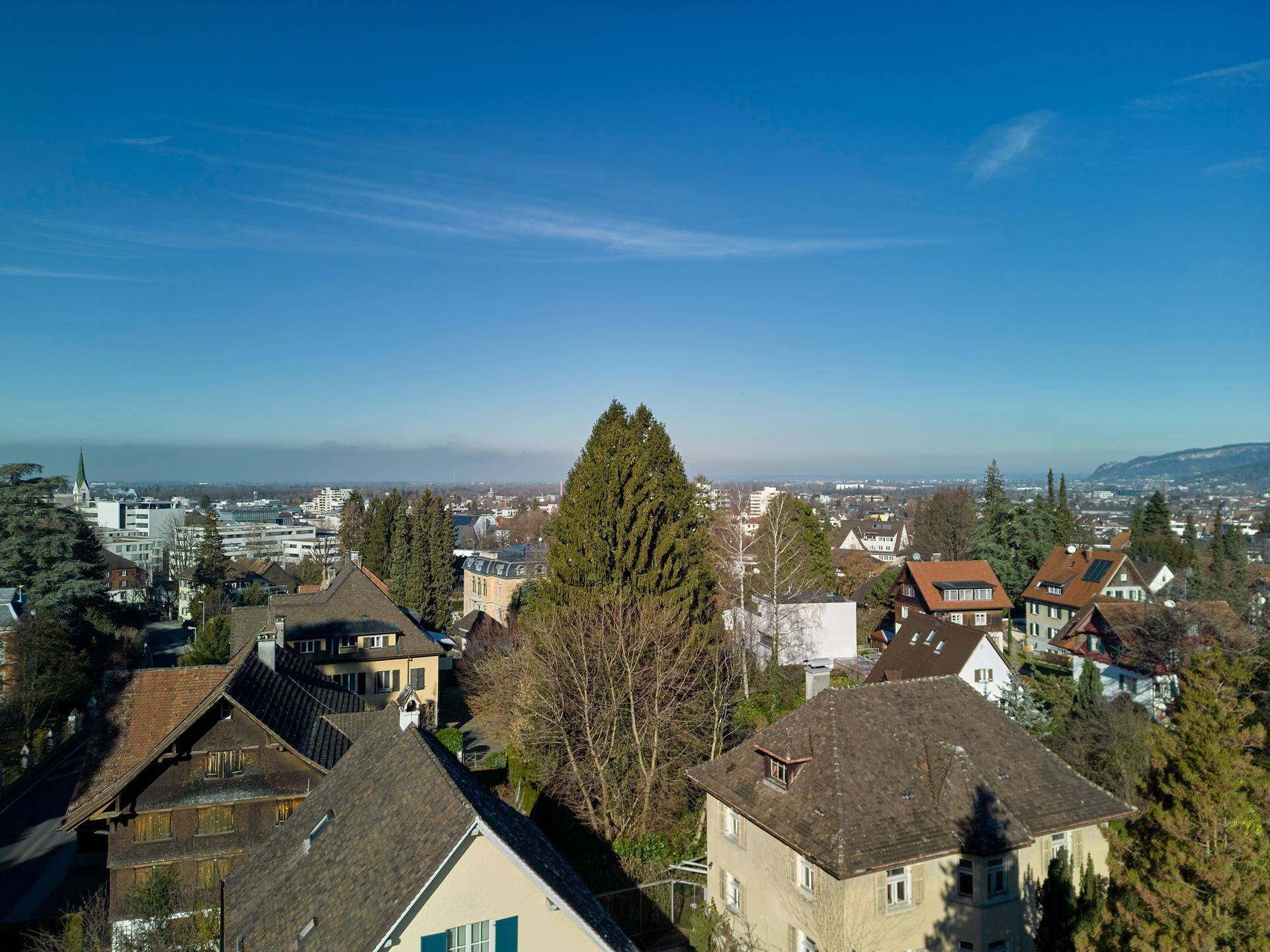 Luftaufnahme einer Wohngegend mit Häusern und Blick auf die Stadt und ferne Berge unter blauem Himmel.