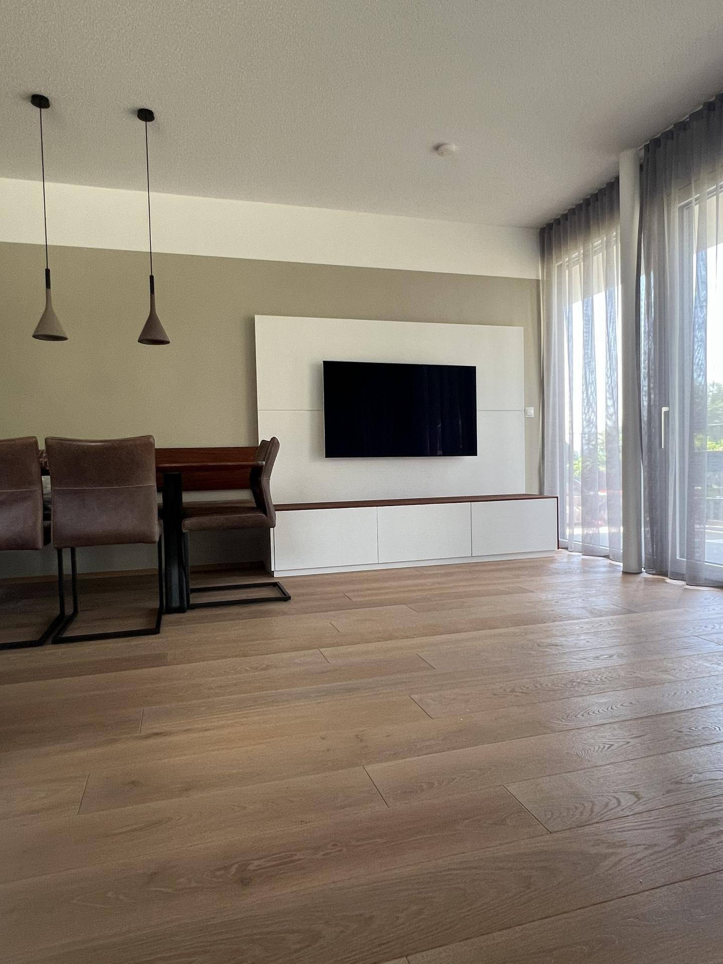 Offener Essbereich mit TV-Wand und großen Fenstern, die viel Licht hereinlassen.