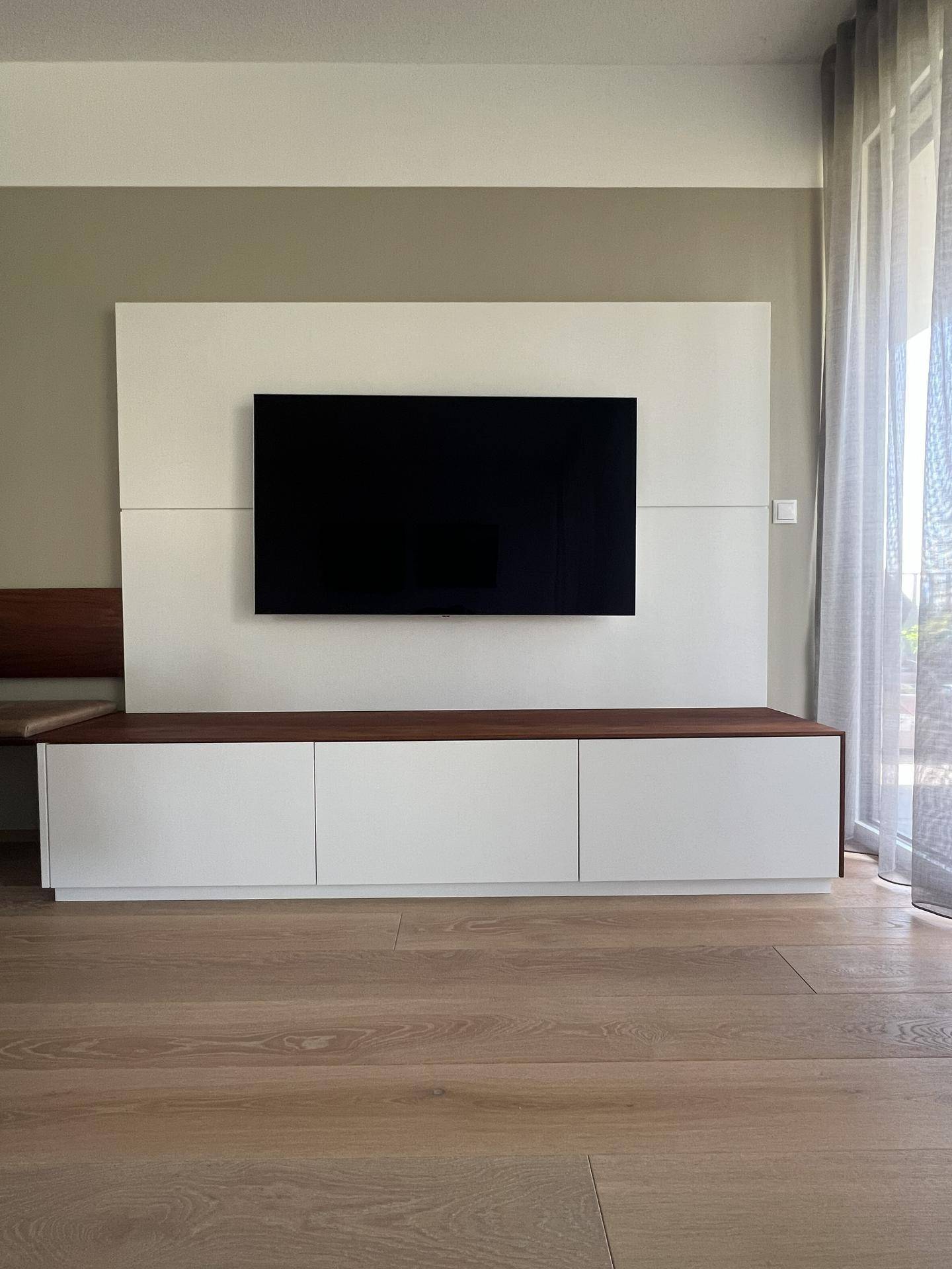 Moderner TV-Wandbereich mit Flachbildschirm und minimalistischem Unterschrank in Weiß.