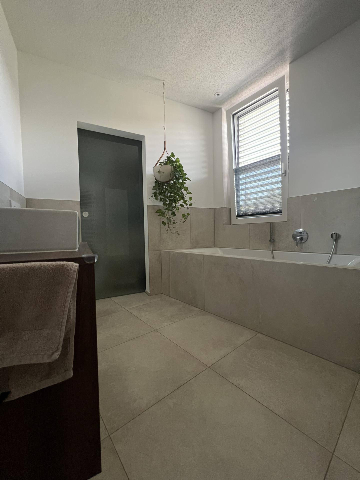 Modernes Badezimmer mit eingebauter Badewanne, großen Fliesen und Fenster für Tageslicht.
