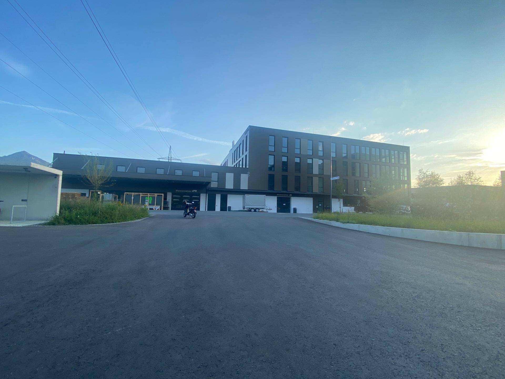 Weitläufige Ansicht eines modernen Bürokomplexes mit Parkplätzen und bergiger Landschaft im Hintergrund.